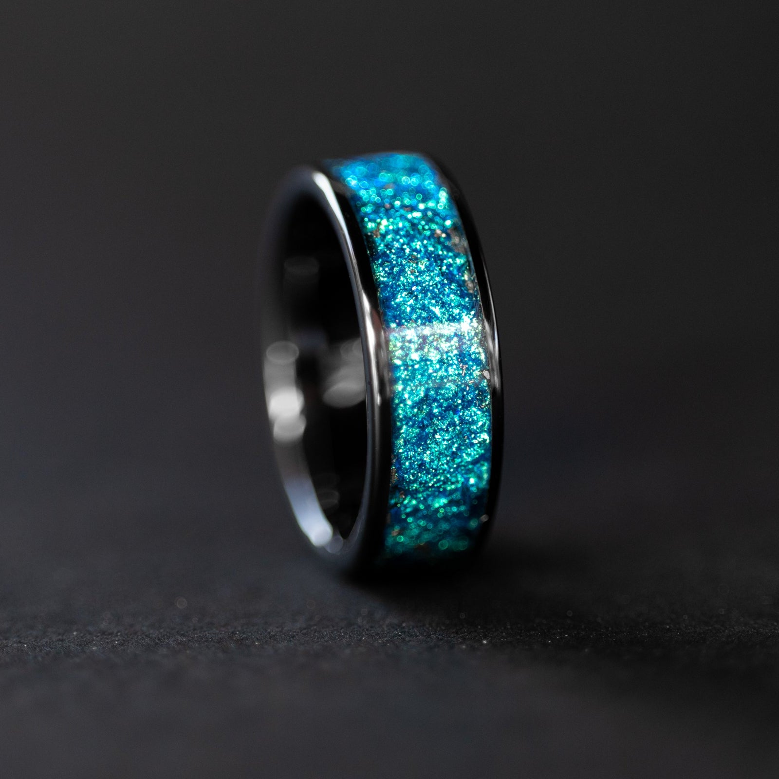 Close up of genuine Campo del Cielo meteorite shavings suspended in rich blue glitter pigment inlay on wide channel black ceramic ring