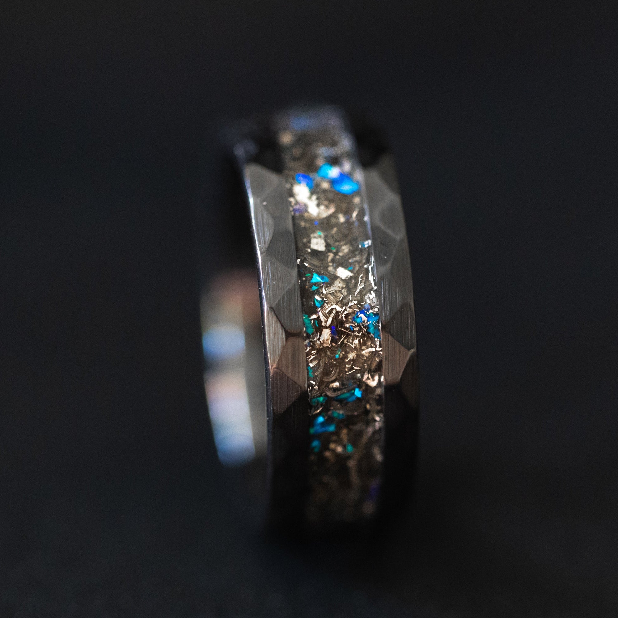 Close up of genuine Campo del Cielo meteorite shavings with scattered blue opal accents on hammered black ceramic ring