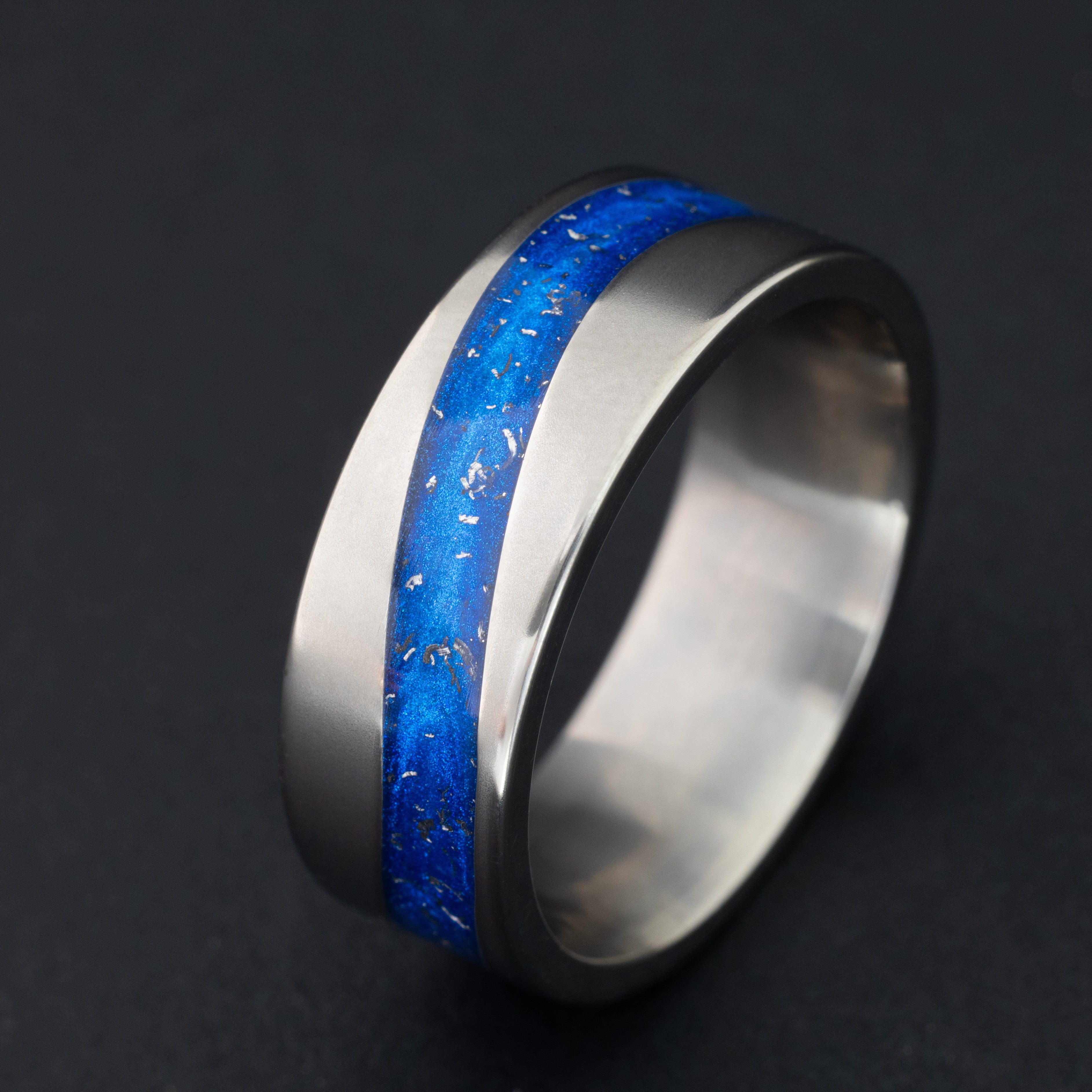Close up of genuine Campo del Cielo meteorite pieces suspended in blue resin following the curved inlay channel on tungsten ring