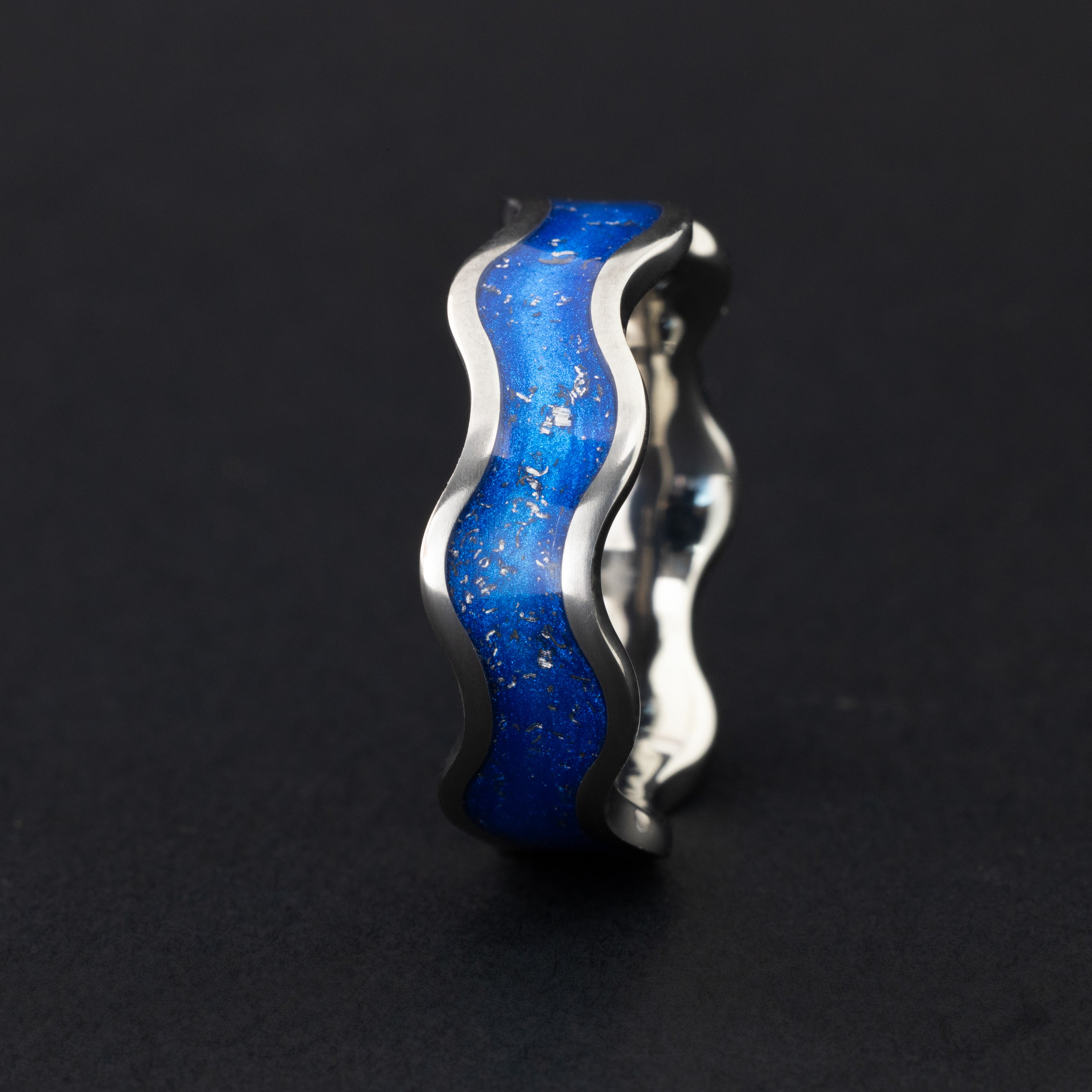 Close up of genuine Campo del Cielo meteorite pieces suspended in blue resin inlay following the wave profile of the titanium wiggle band