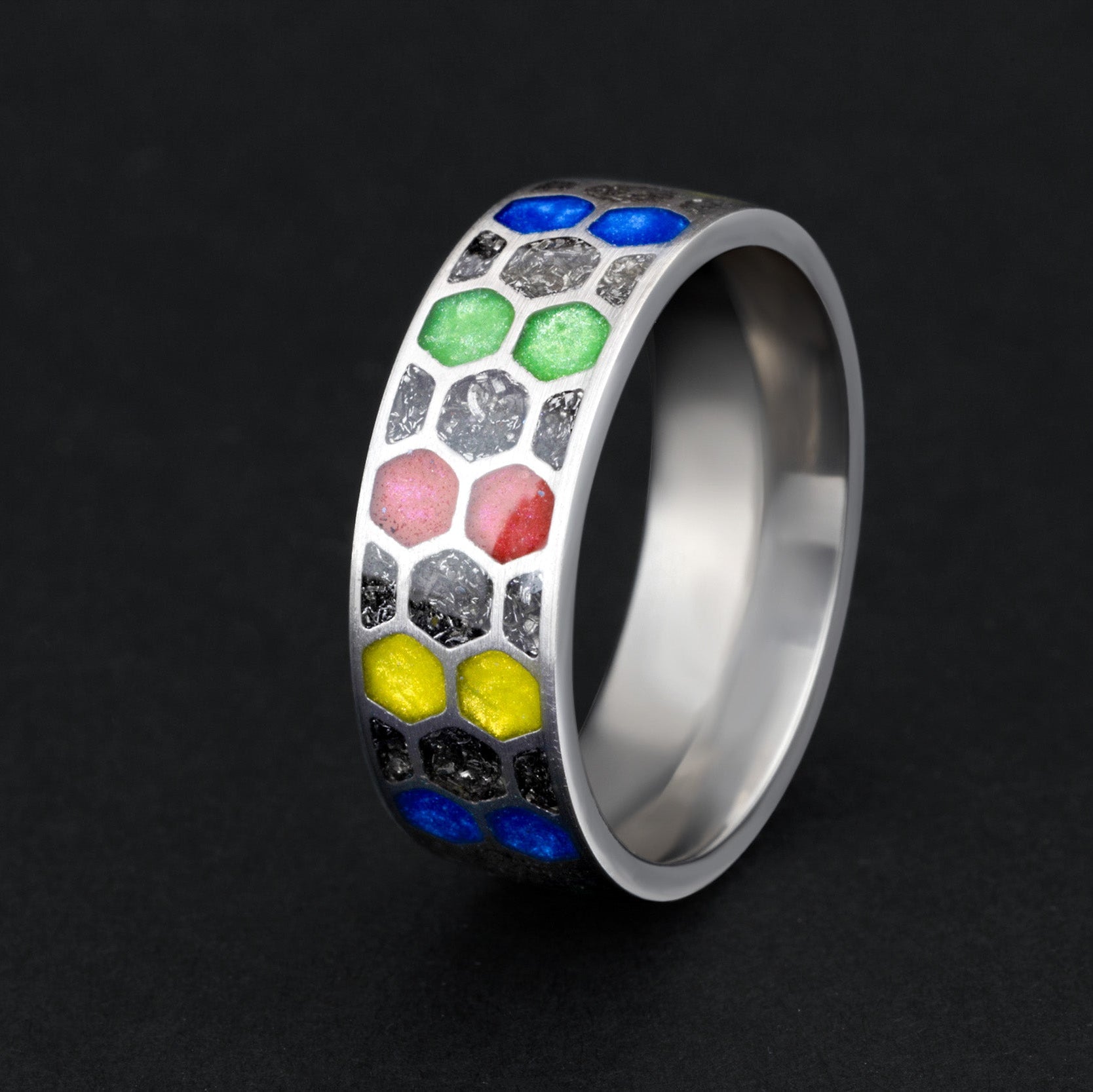 Close up of genuine Campo del Cielo meteorite dust and vibrant red blue yellow green resin in individual honeycomb cells on titanium ring