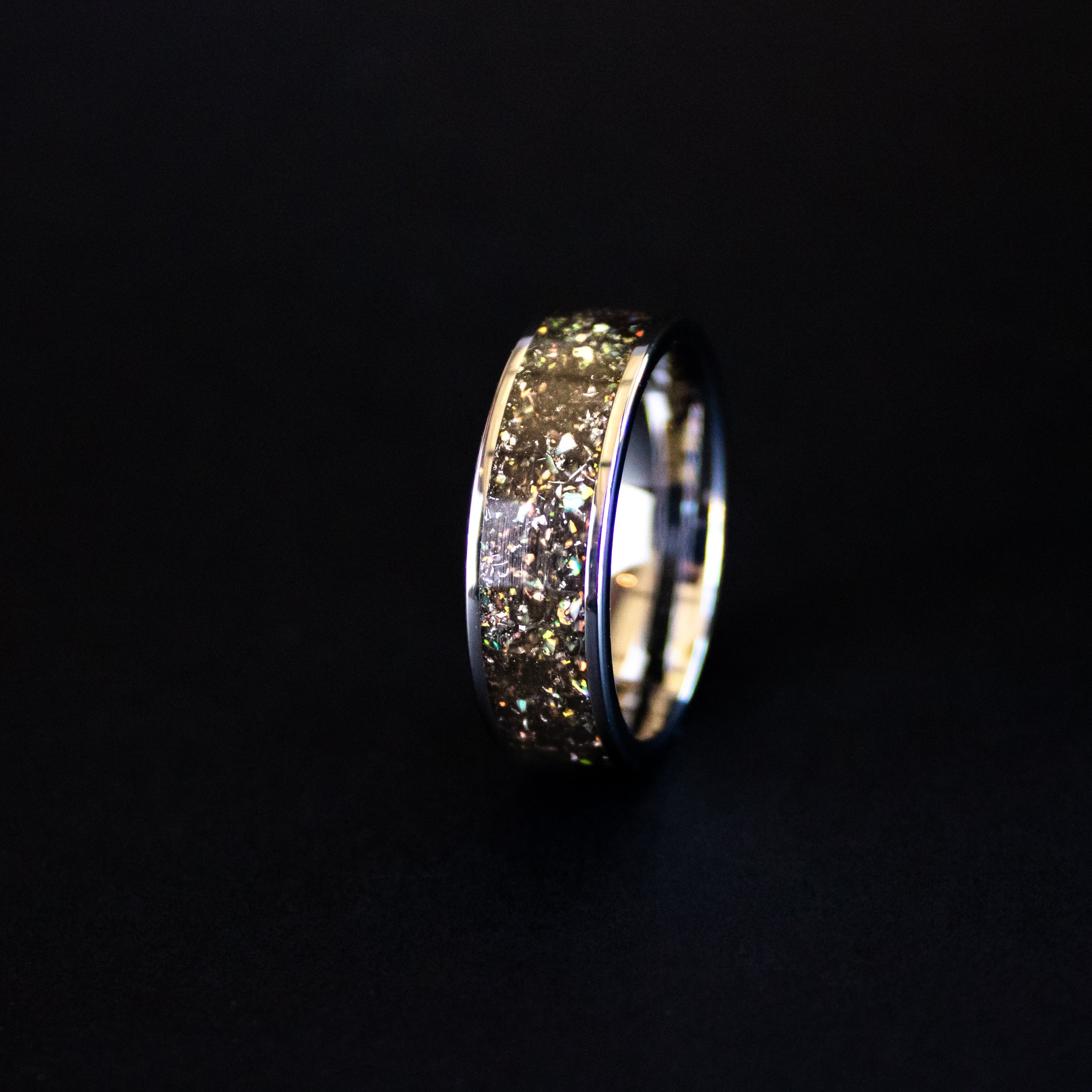 Close up of genuine Campo del Cielo meteorite shavings with scattered white rainbow iridescent opal accents on wide channel tungsten ring