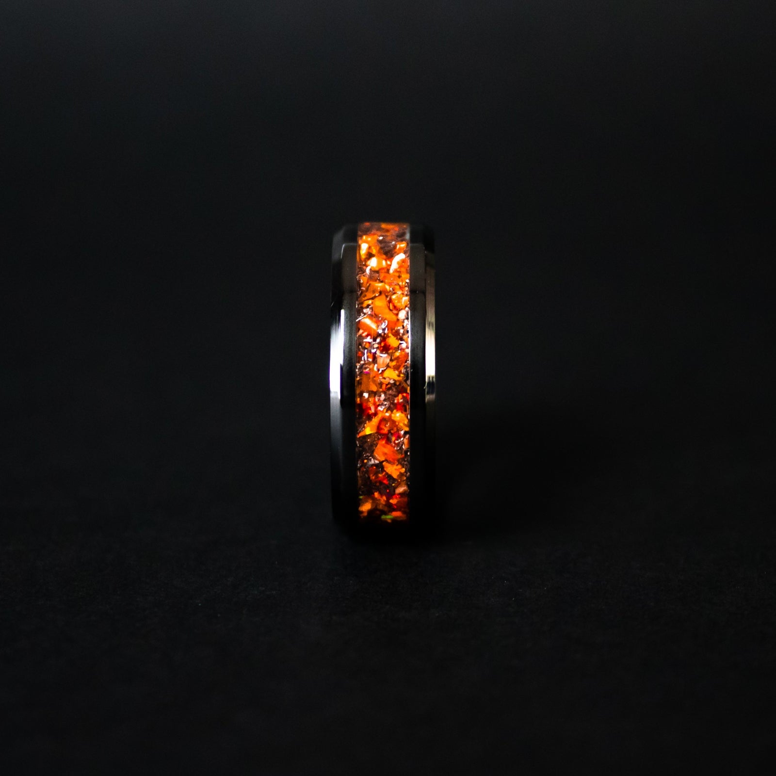 Close up of genuine Campo del Cielo meteorite shavings suspended in premium orange opal inlay on beveled black ceramic ring