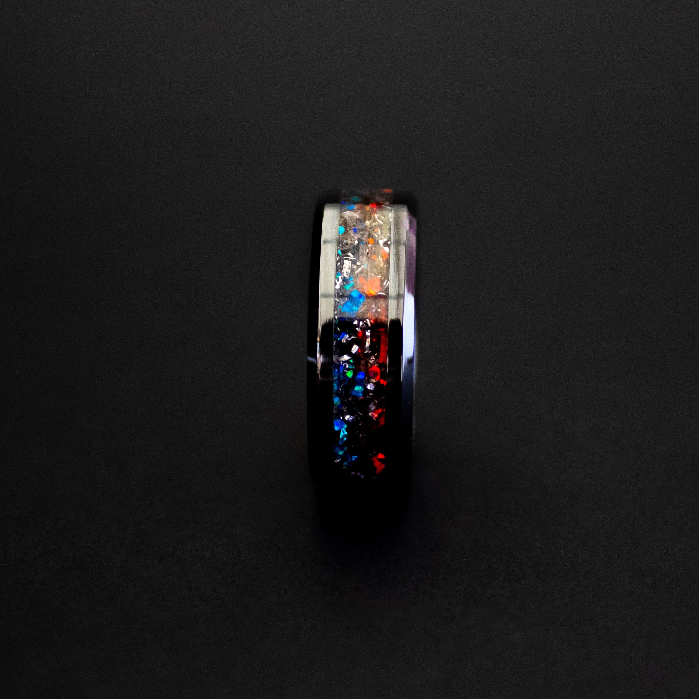 Close up of genuine Campo del Cielo meteorite shavings scattered across split red and blue opal inlay on beveled black ceramic ring