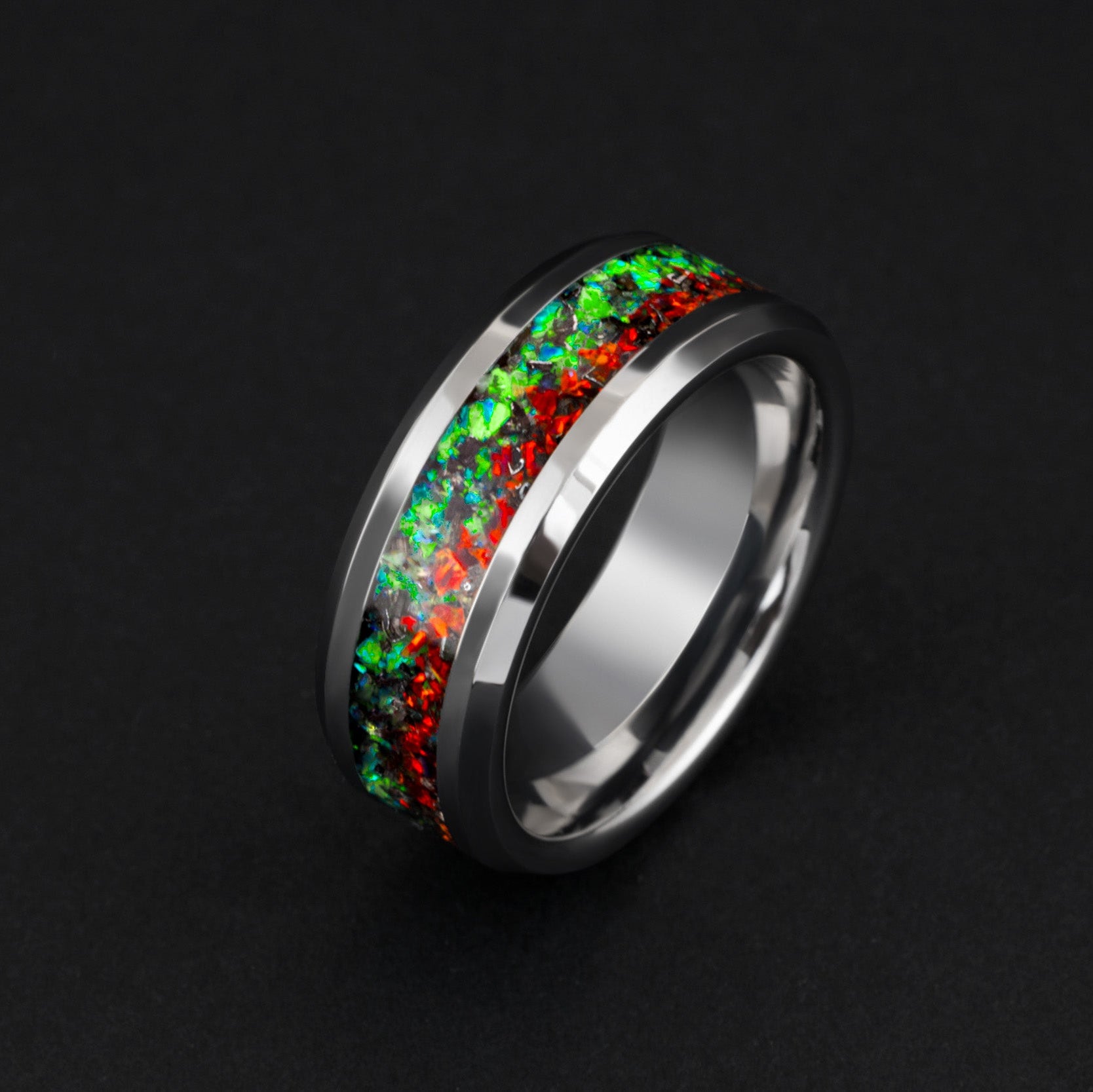 Close up of genuine Campo del Cielo meteorite shavings scattered across split red and green opal inlay on beveled tungsten ring