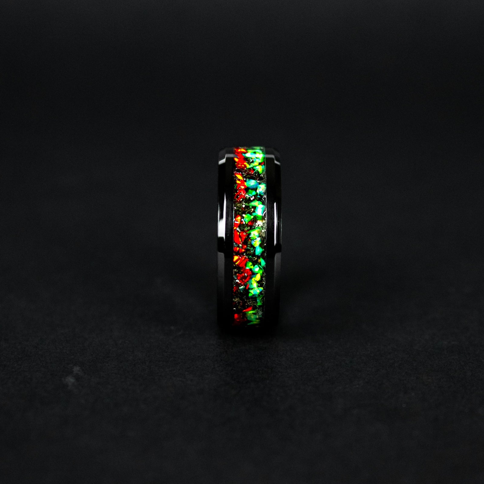Close up of genuine Campo del Cielo meteorite shavings scattered across split red and green opal inlay on beveled black ceramic ring