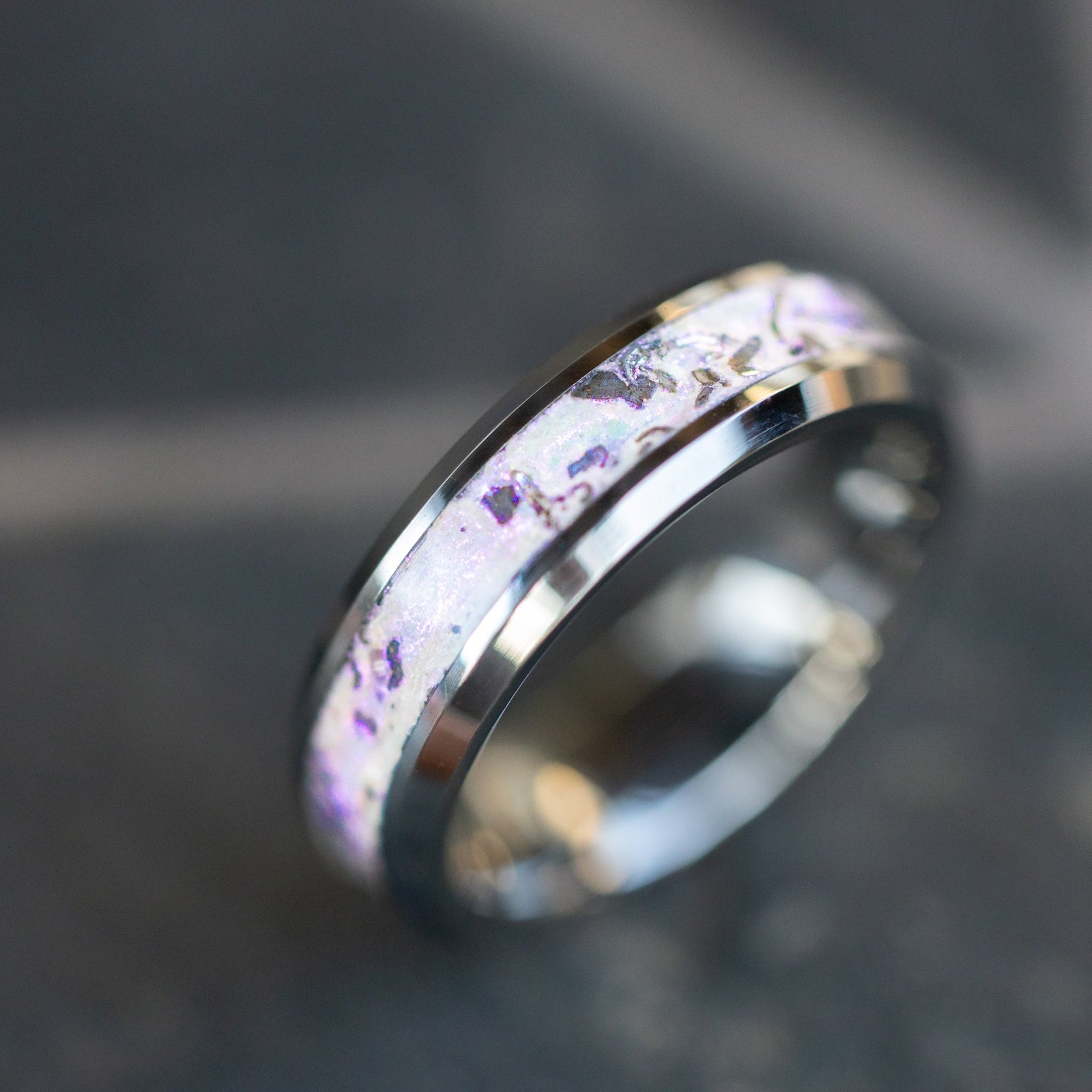 Close up of genuine Campo del Cielo meteorite shavings suspended in white pearl glitter with subtle rose sheen on beveled tungsten ring