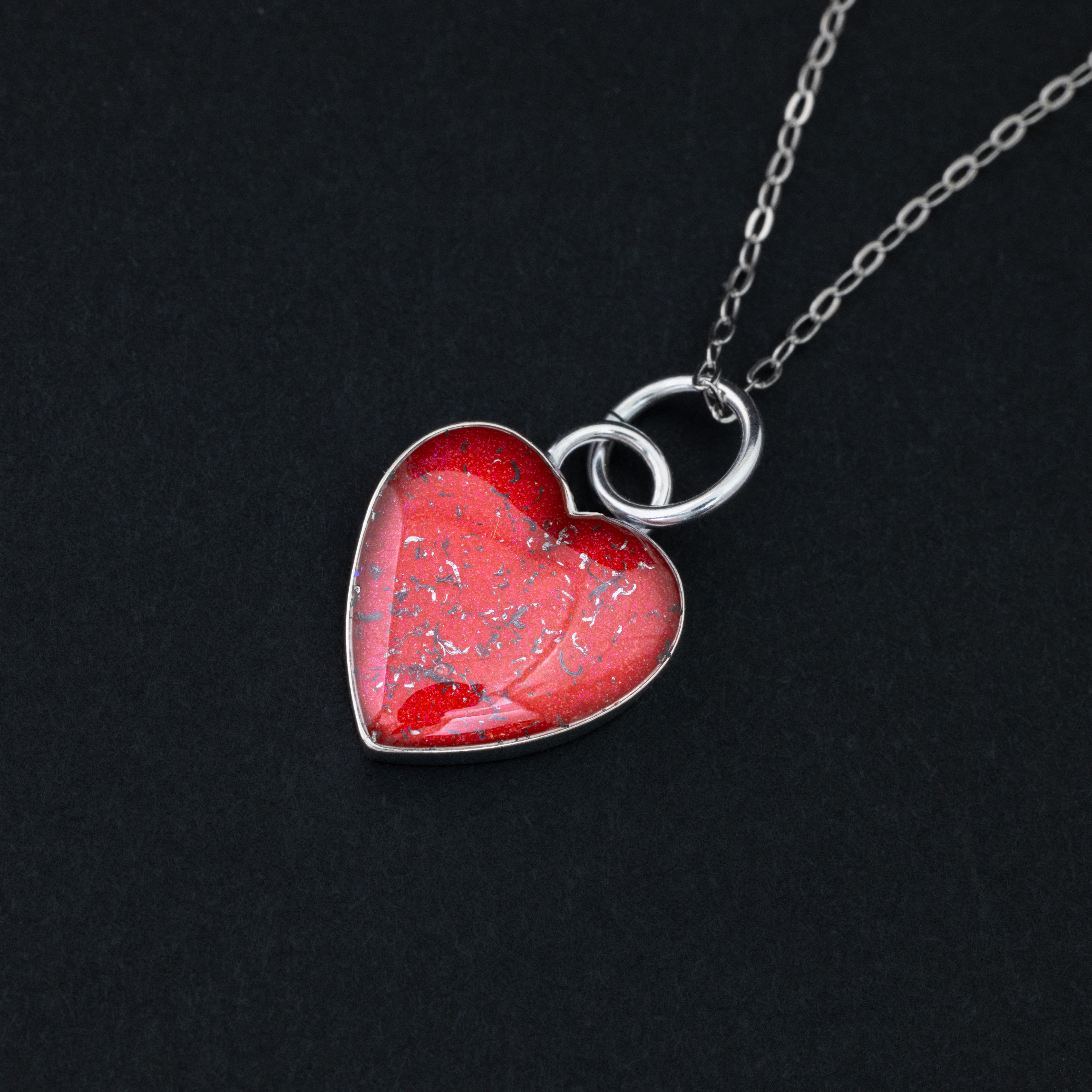 Close-up of the Cherry Pulse red heart necklace showing Campo Del Cielo iron meteorite fragments set in deep cherry red resin