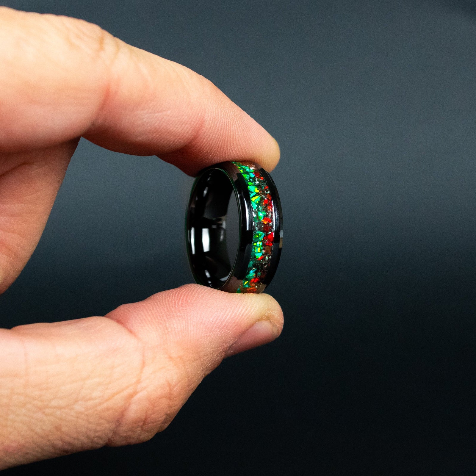 Detail shot of the Christmas Meteorite ring showing authentic Campo del Cielo meteorite shavings bridging the transition between red and green opal halves on black ceramic band