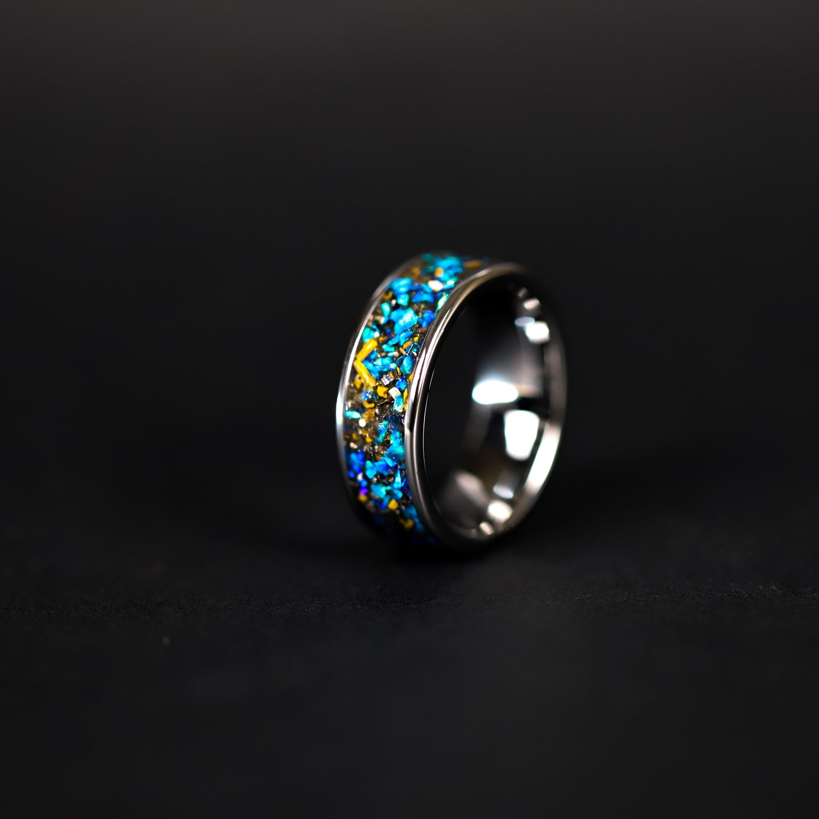 Detail shot of the Cobalt Velociraptor Wide ring showing authentic Velociraptor bone fragments and meteorite shavings catching light through blue opal inlay on wide channel tungsten band