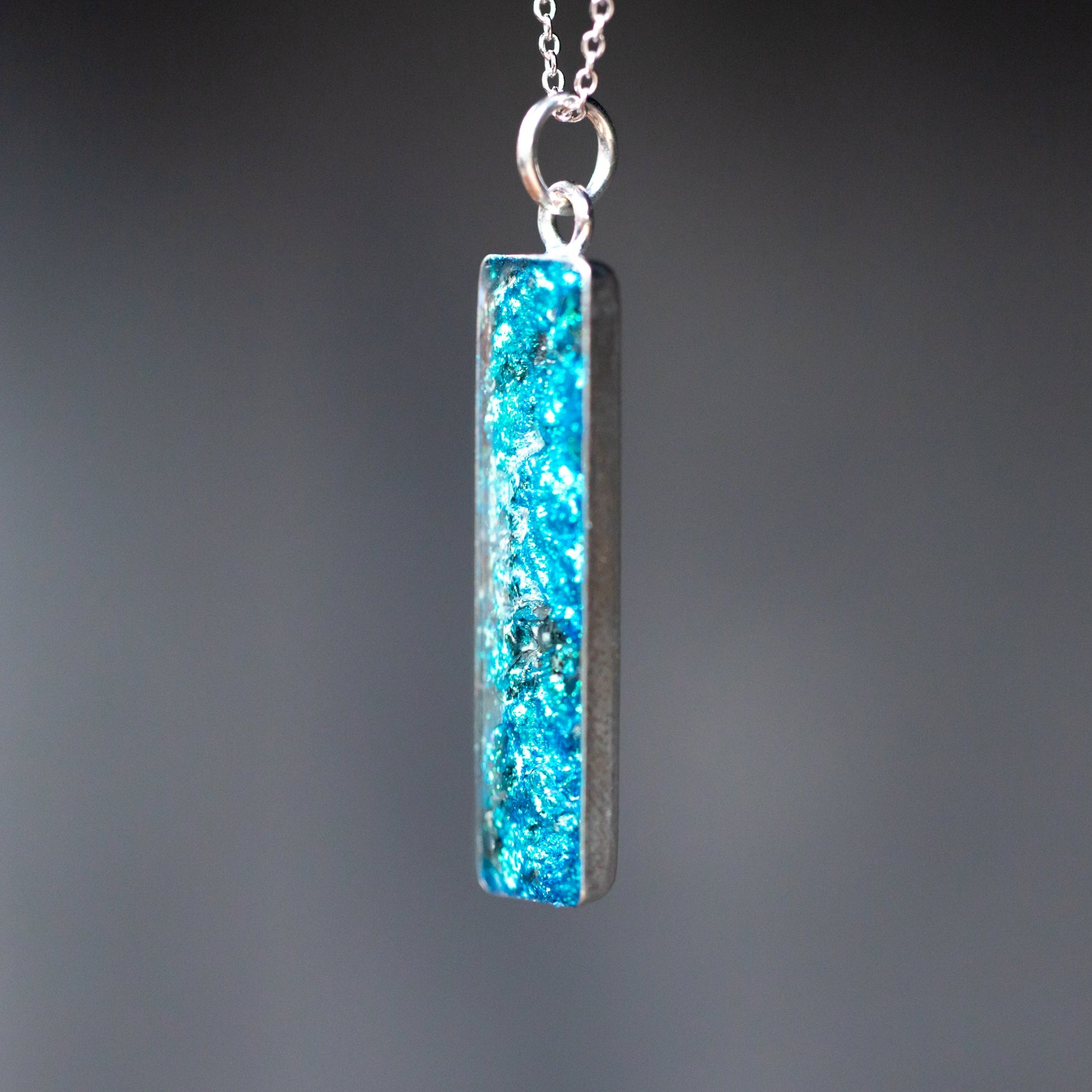 Close-up of the Comet Sky blue bar necklace showing Campo Del Cielo iron meteorite fragments set in deep blue glitter pigment