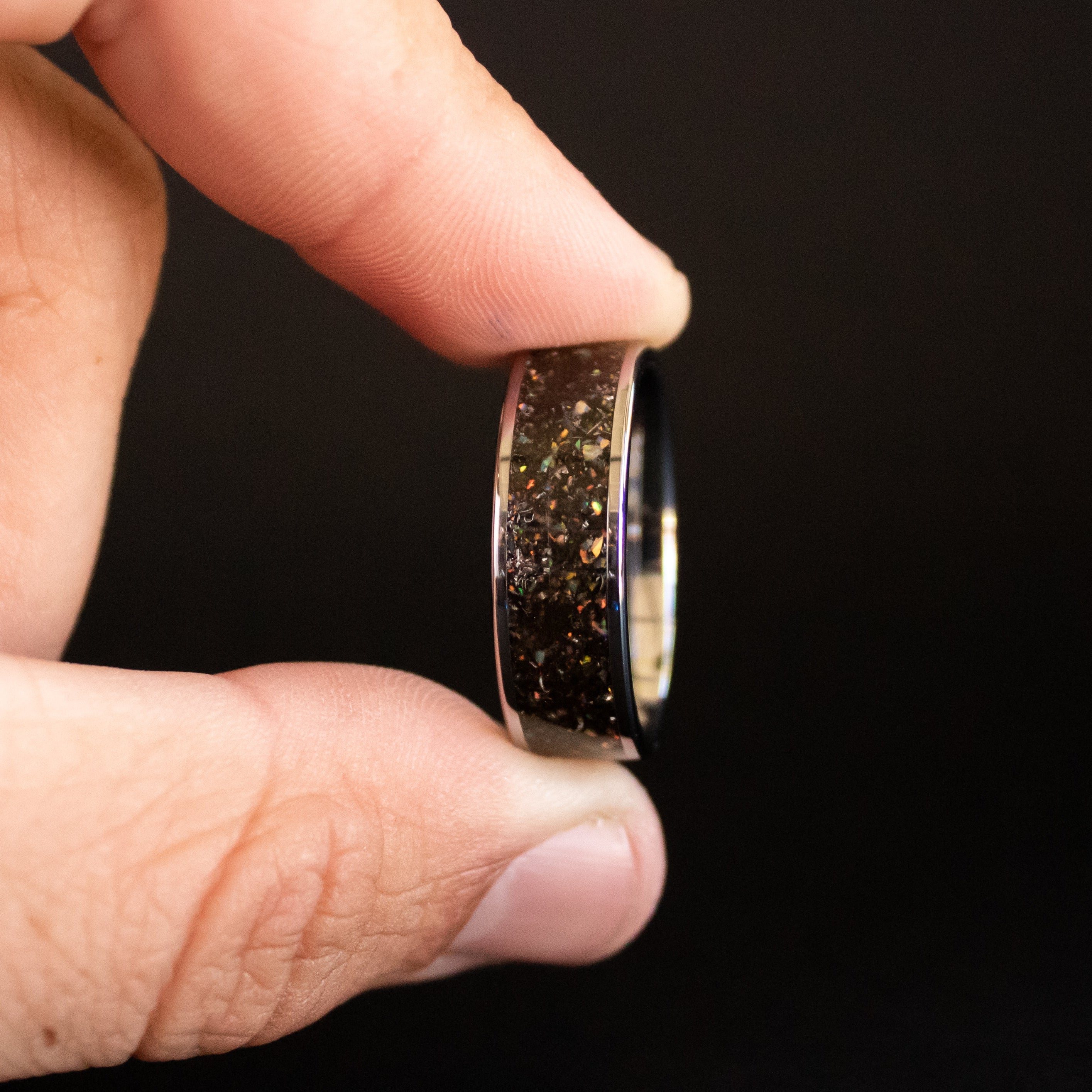 Detail shot of the Cosmic Pearl Tungsten ring showing authentic Campo del Cielo meteorite shavings and white rainbow iridescent opal accents catching light on wide channel tungsten band