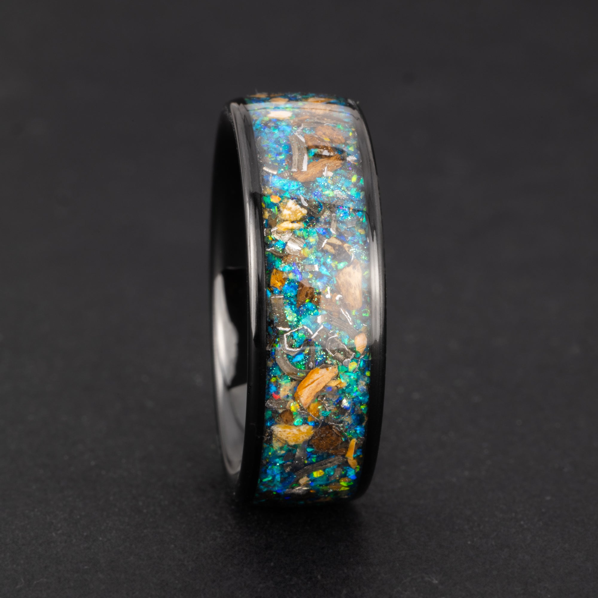 Close-up of the Cosmic Predator Ring showing Campo Del Cielo iron meteorite, real T-Rex bone, real velociraptor bone, and a galaxy blend of blue, green, and purple opals and pigment glitter in black ceramic