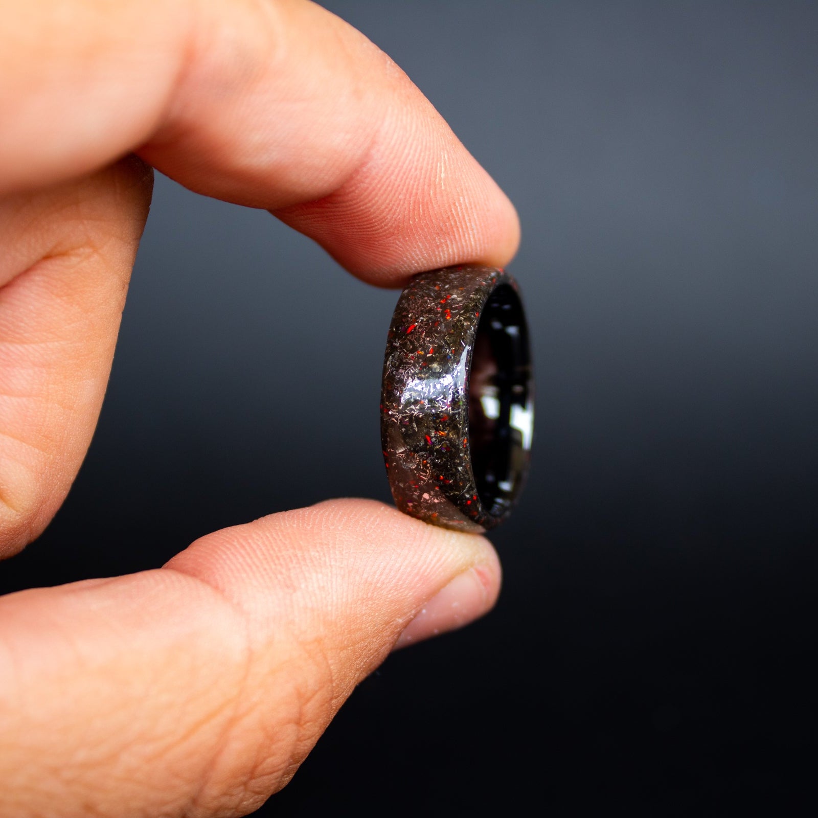 Detail shot of the Crimson Iron ring showing authentic Campo del Cielo meteorite shavings and subtle red opal accents catching light on endless black ceramic band