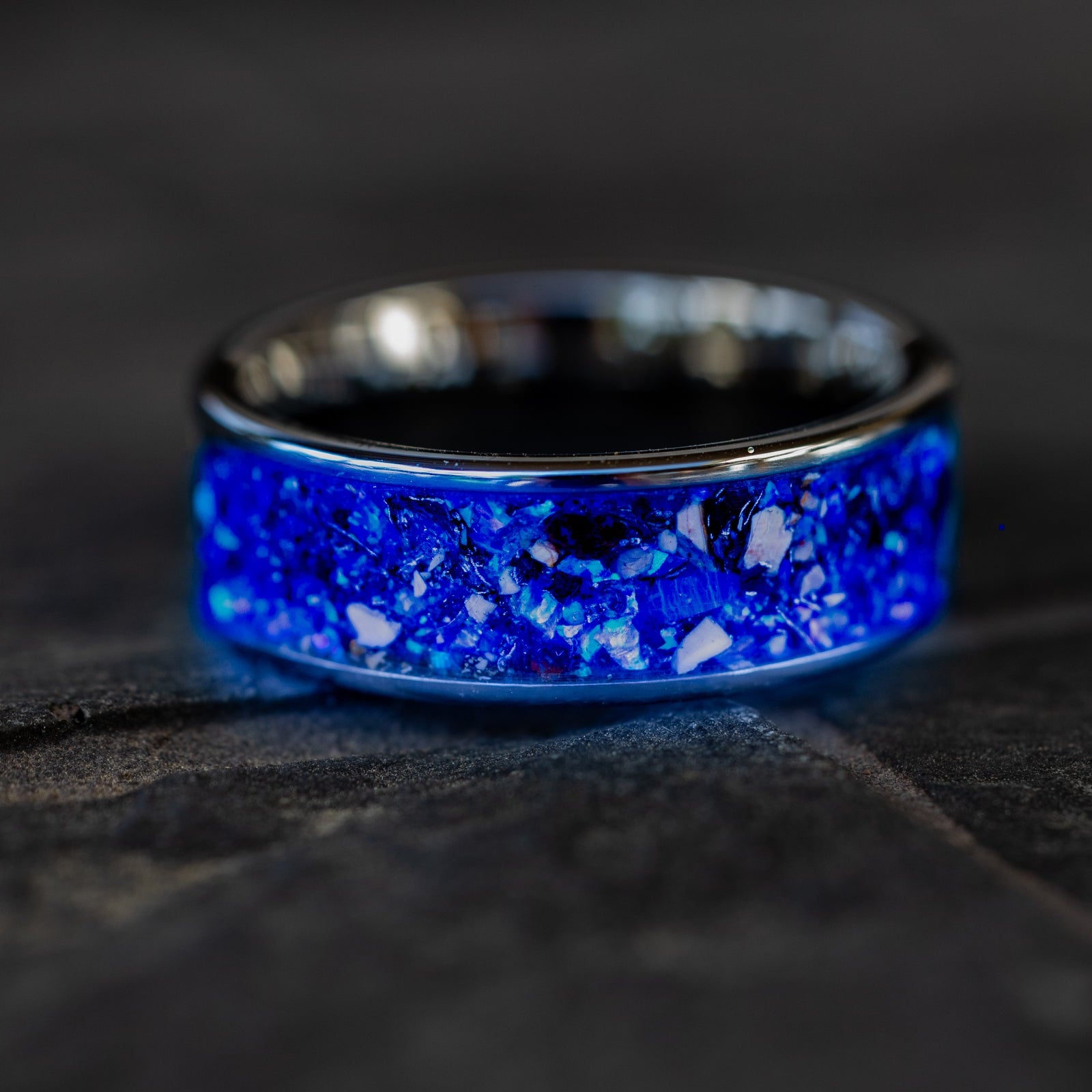 Deep Origin Glow ring glowing blue in total darkness showing Mosasaur bone, Dinosaur Gembone, and meteorite suspended in electric blue glow in the dark inlay
