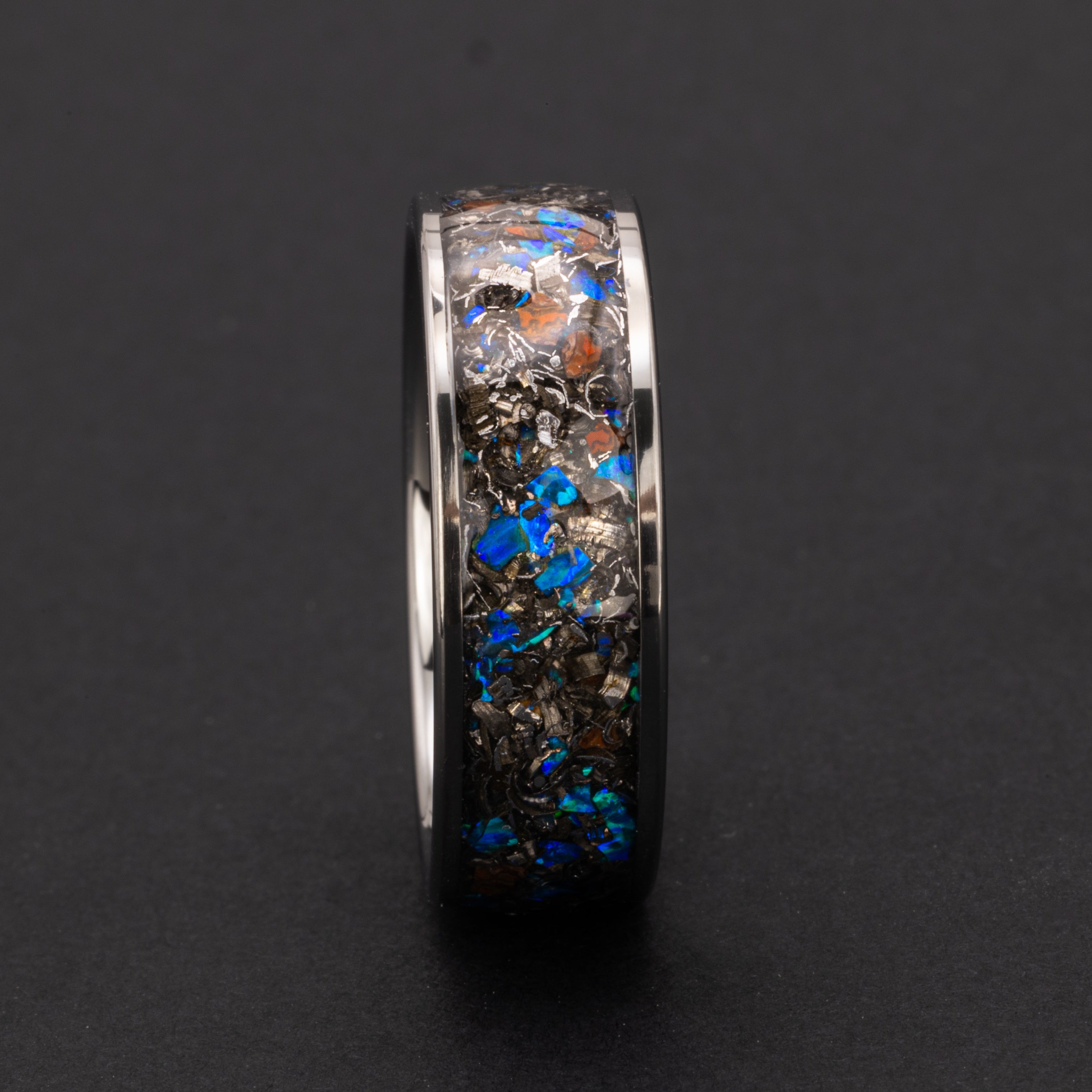 Close up of genuine Dinosaur Gembone and Campo del Cielo meteorite shavings with scattered blue opal accents on wide channel tungsten ring