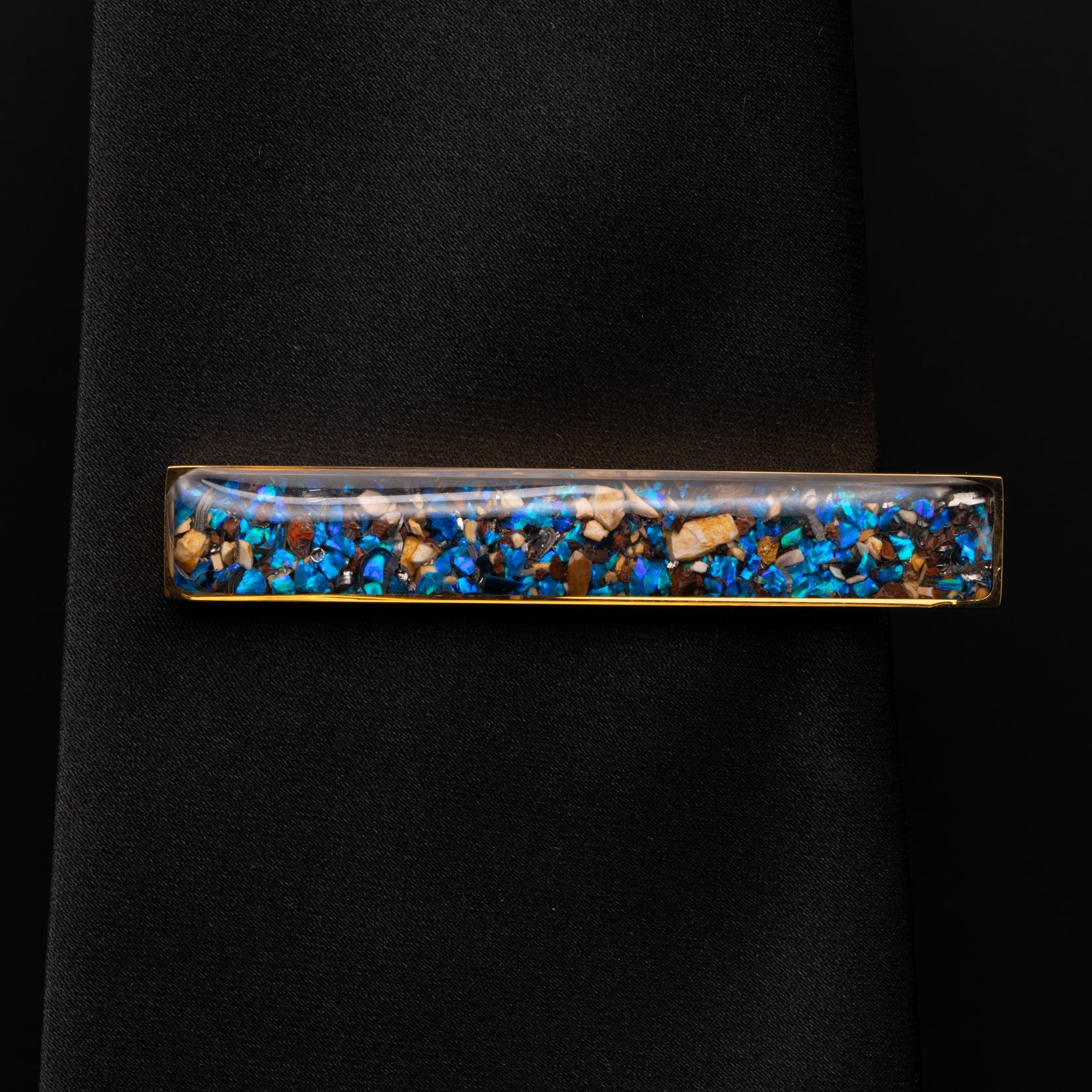 Close-up of the Dinosaur Meteorite Tie Clip showing Campo Del Cielo iron meteorite, real dinosaur bone, agatized dinosaur gembone, and blue opal set in polished gold-tone stainless steel