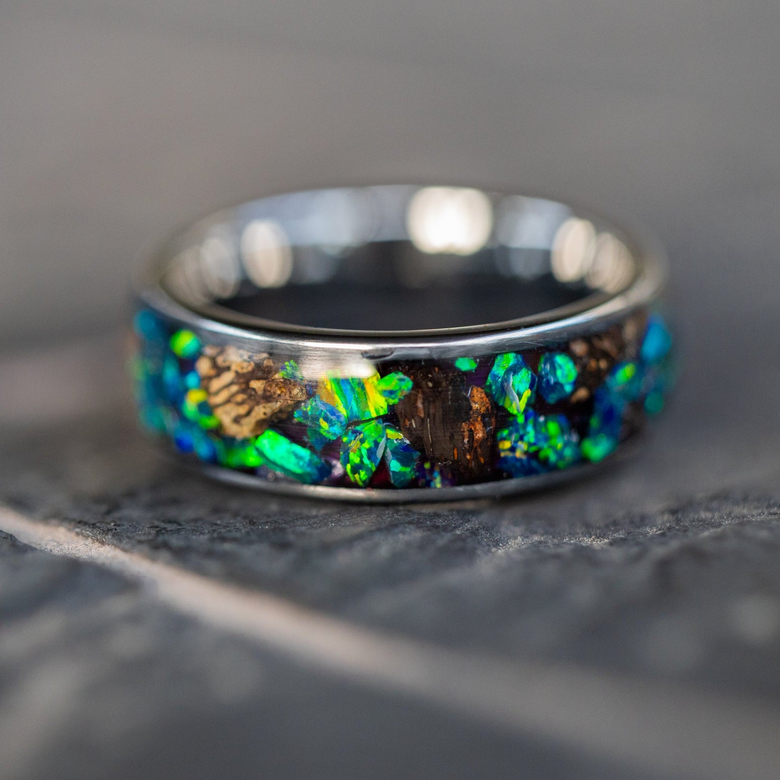 Detail shot of the Epic Rex Lagoon ring showing large authentic T-Rex bone pieces catching light through blue and green opal inlay on wide channel tungsten band