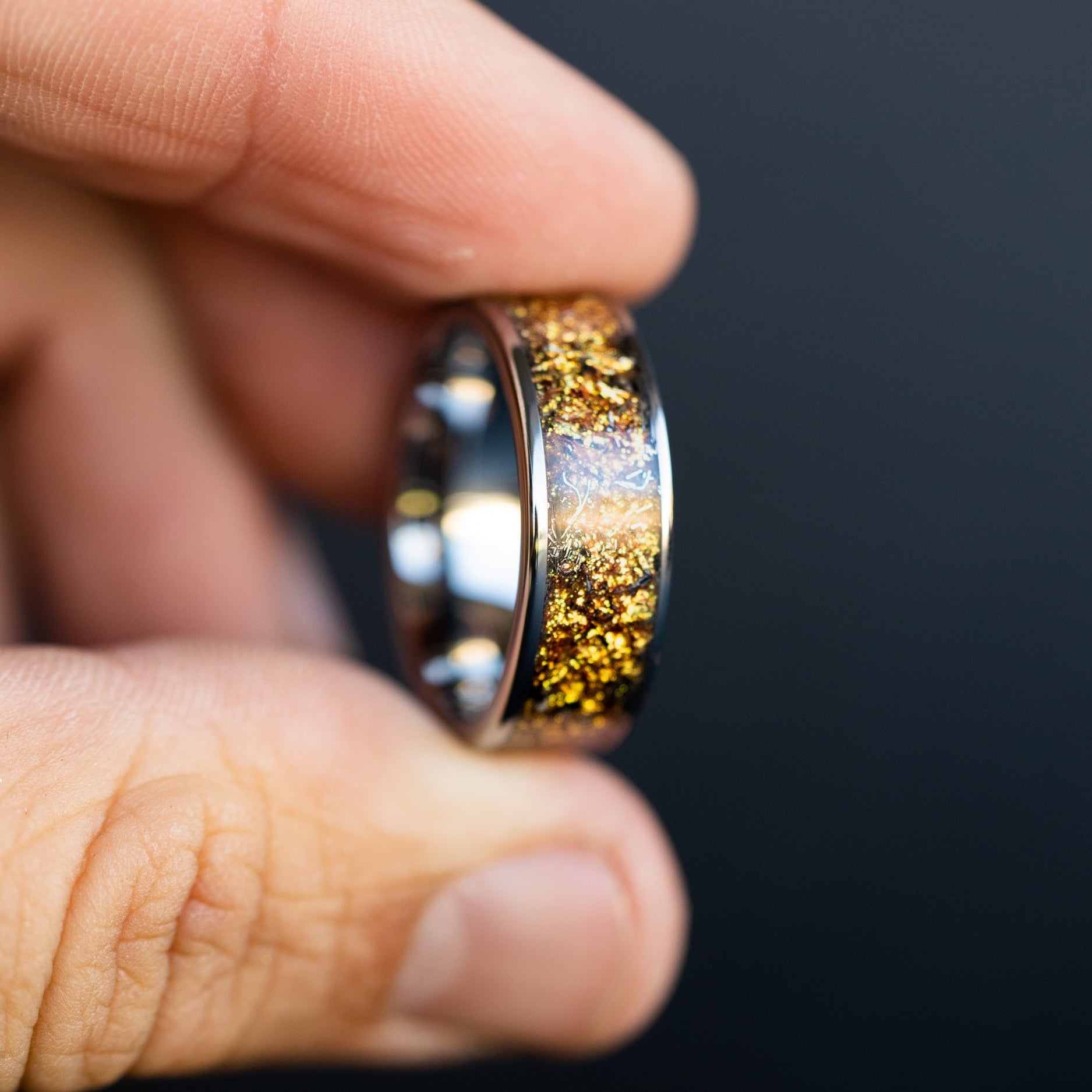 Detail shot of the Gilded Cosmos Tungsten ring showing authentic Campo del Cielo meteorite shavings catching light through warm gold galaxy pigment inlay