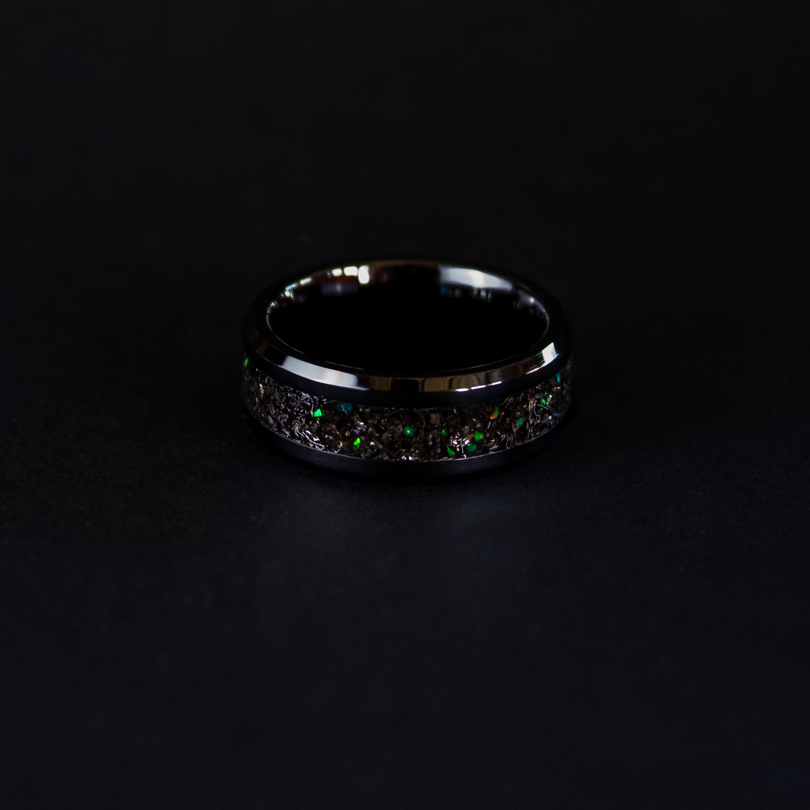 Detail shot of the Green Spark Ceramic ring showing authentic Gibeon meteorite shavings and green opal accents catching light on beveled black ceramic band