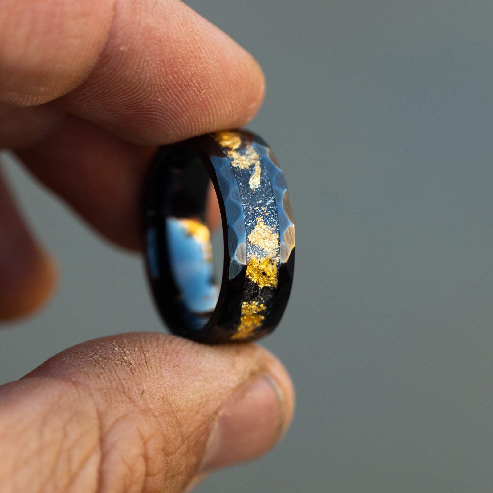Detail shot of the Hammered Gold ring showing authentic Campo del Cielo meteorite shavings and delicate gold leaf catching light on hammered black ceramic band