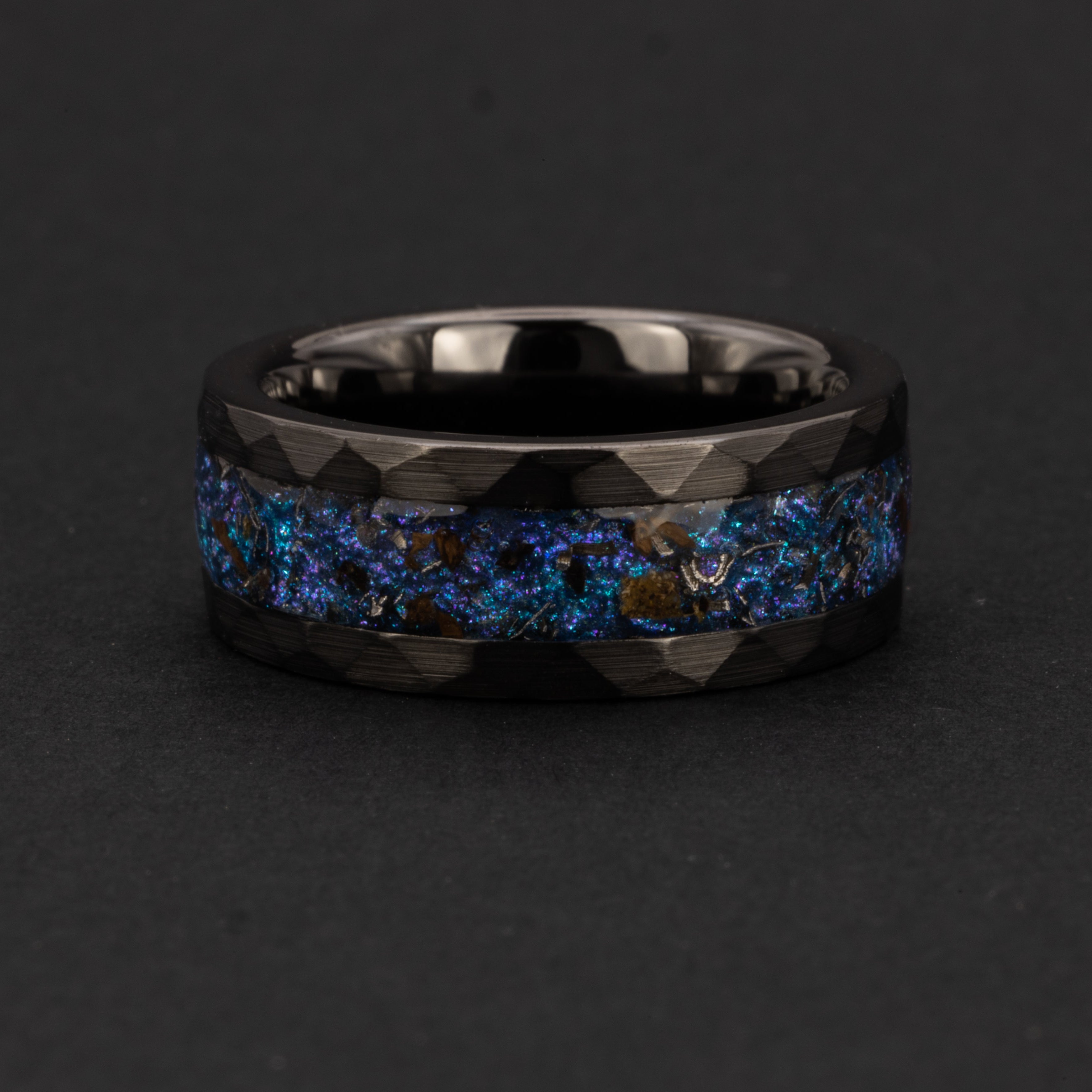 Detail shot of the Hammered Rex Galaxy ring showing authentic T-Rex bone fragments and meteorite shavings catching light through blue and purple opal galaxy inlay on hammered black ceramic band