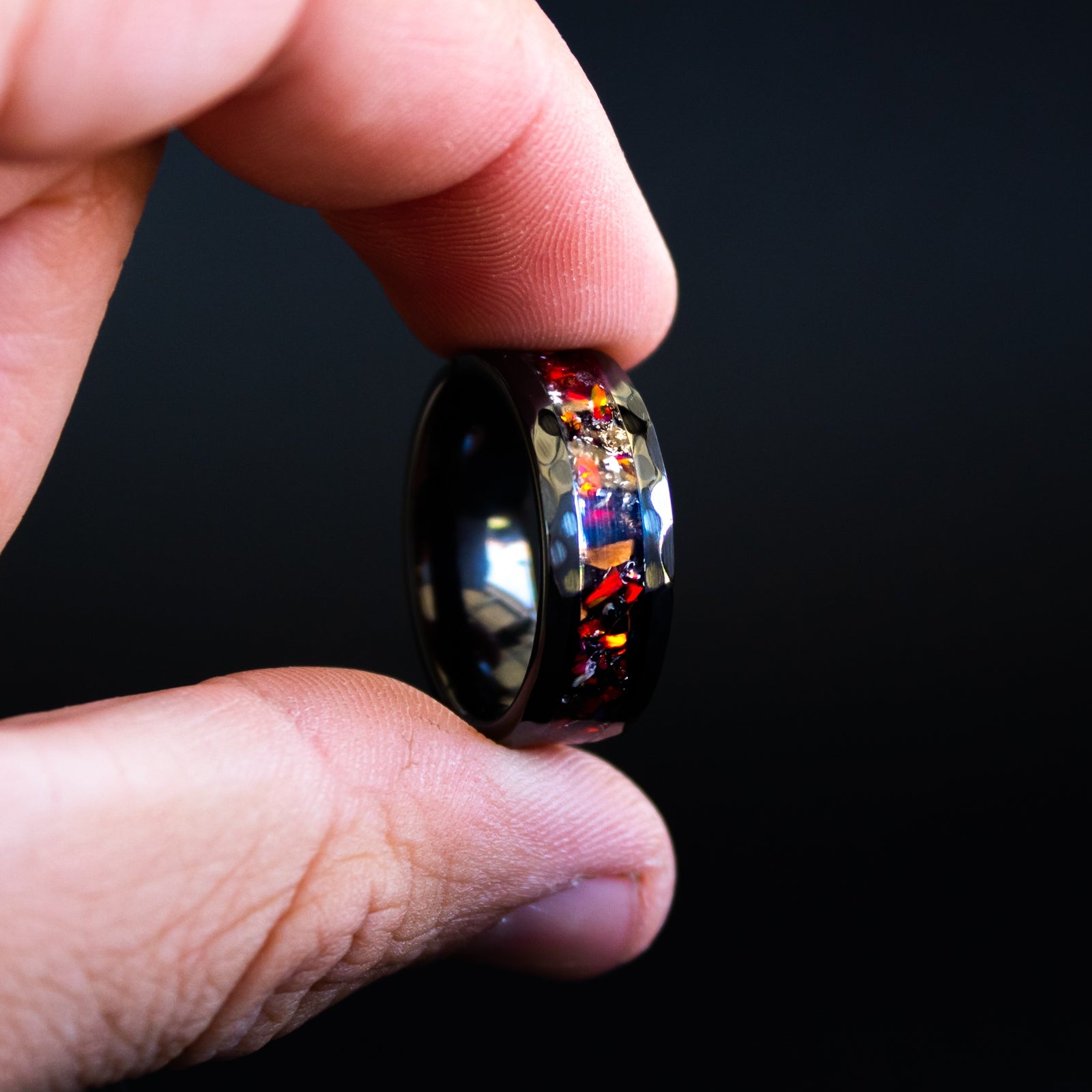 Detail shot of the Hammered Rex ring showing authentic T-Rex bone fragments and meteorite shavings catching light through red opal inlay on hammered black ceramic band