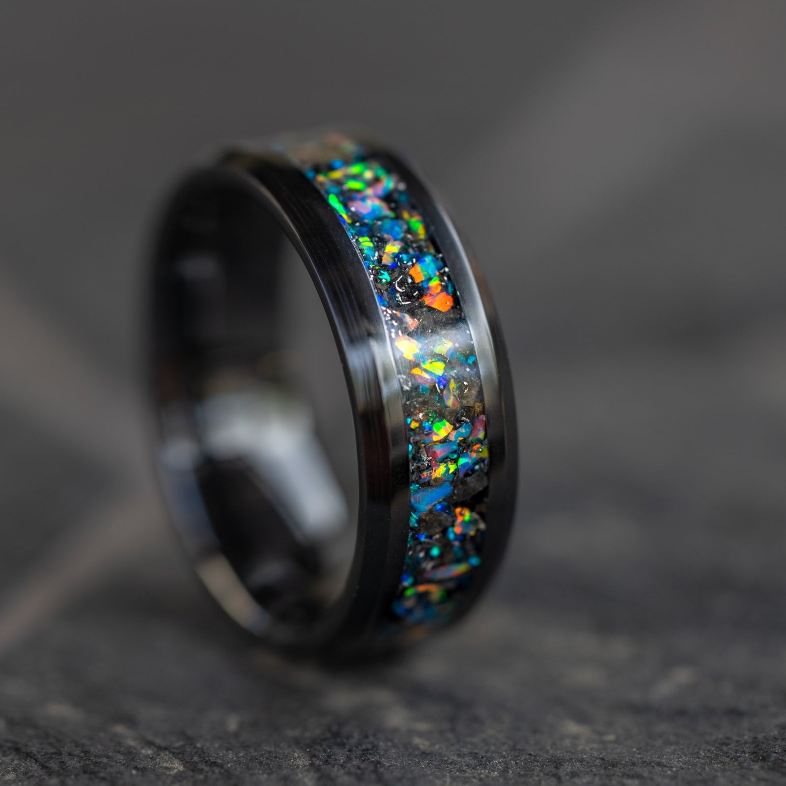 Close up of genuine lunar meteorite pieces surrounded by light gray rainbow moonstone opal inlay on beveled black ceramic ring