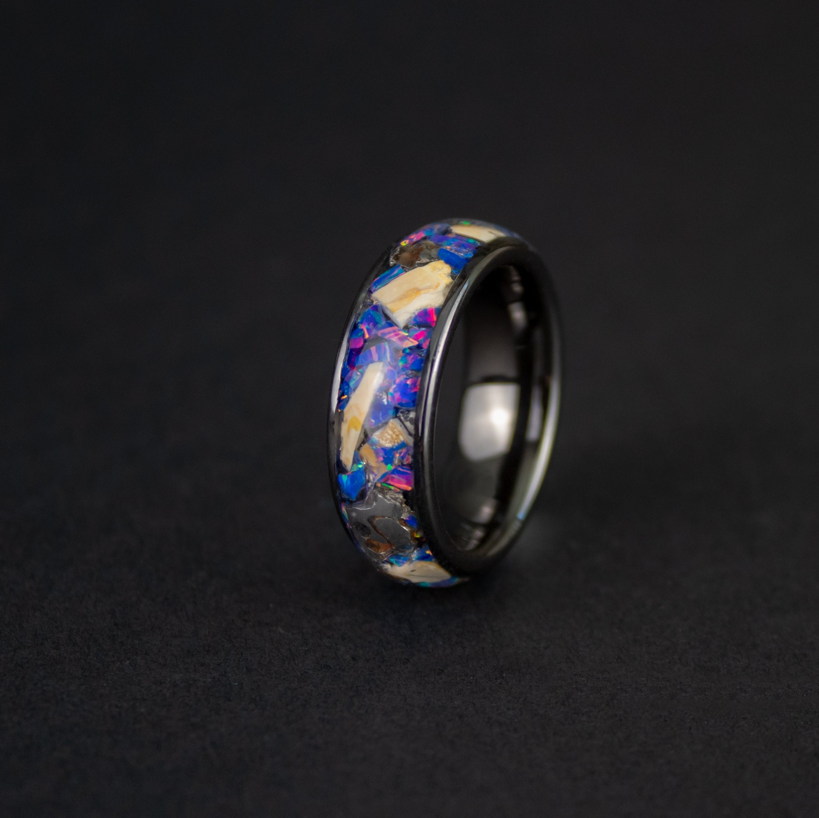 Close up of large genuine Mosasaur fossil pieces and Campo del Cielo meteorite chunks surrounded by midnight blue purple opal inlay on wide channel black ceramic ring