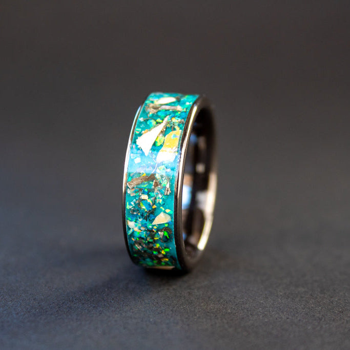 Close up of genuine Mosasaur fossil and Campo del Cielo meteorite shavings suspended in light blue teal oasis opal inlay on wide channel black ceramic ring
