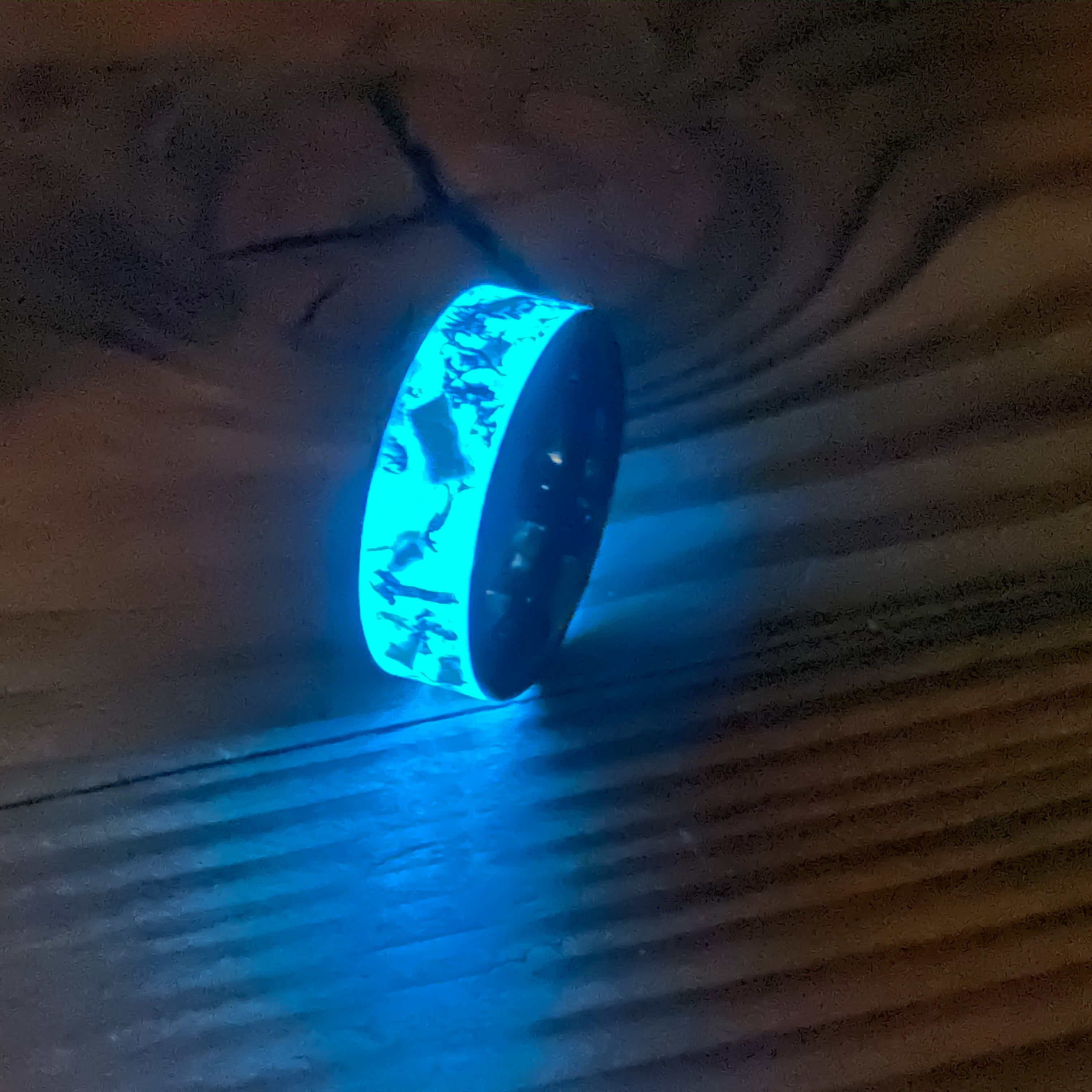 Oasis Mosasaur Glow ring glowing blue in total darkness showing Mosasaur bone and meteorite suspended in electric blue glow in the dark inlay