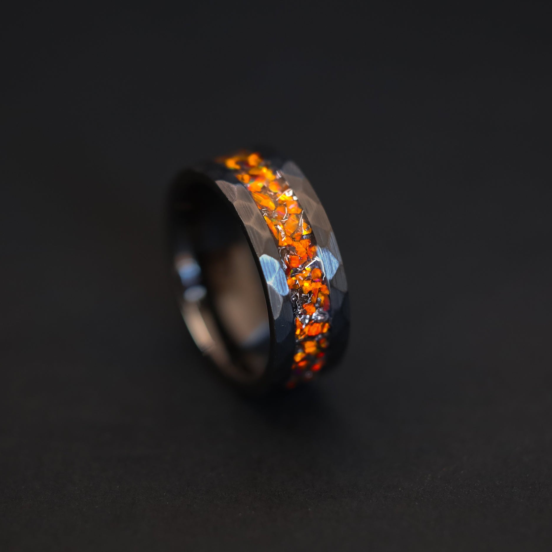 Close up of meteorite shavings and orange opals in a rugged hammered black ceramic ring.