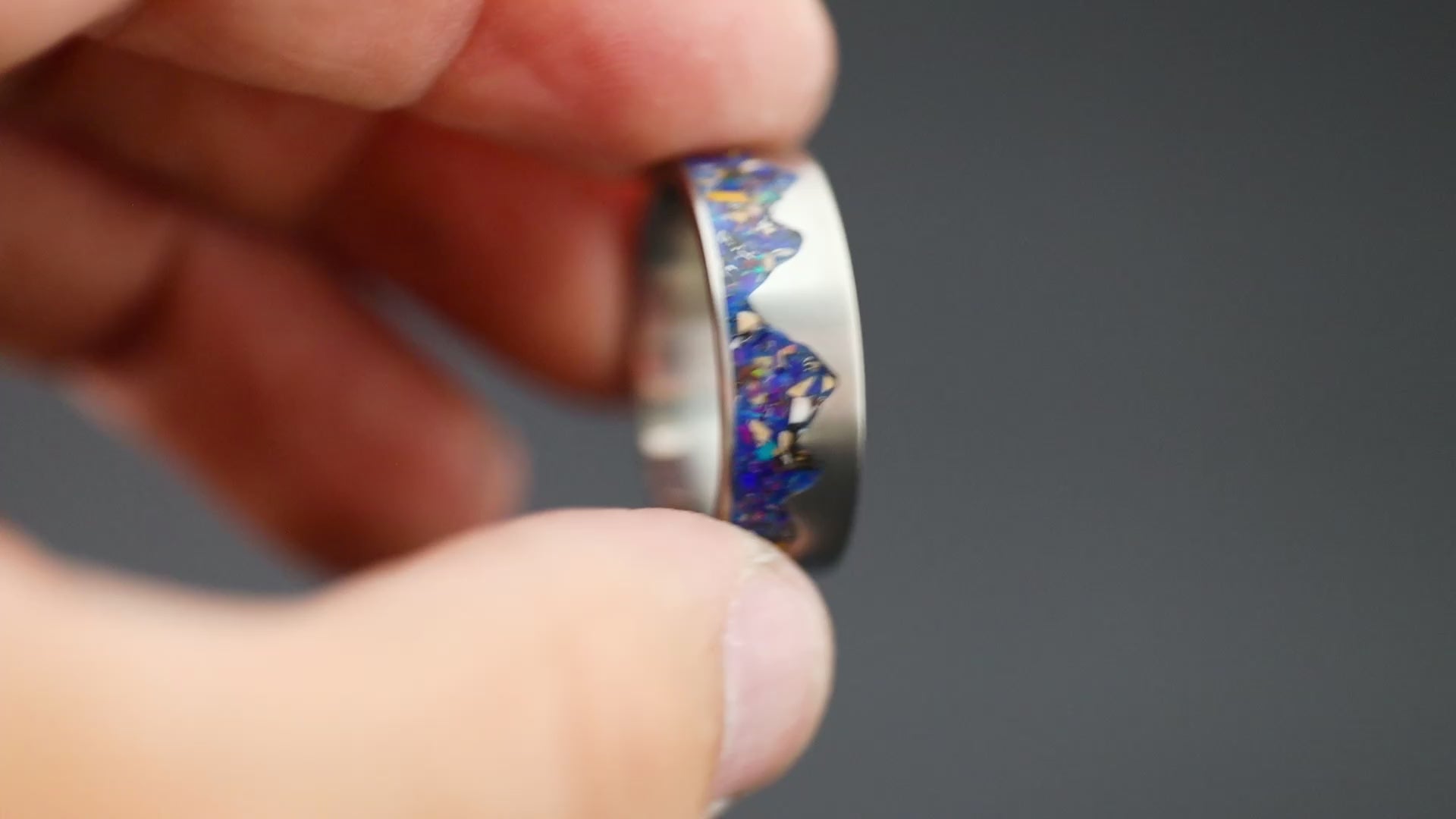 Rotating view of the Raptor Ridgeline Glow titanium ring showing the midnight opal, meteorite, and velociraptor fossil inlay transitioning to its blue glow.