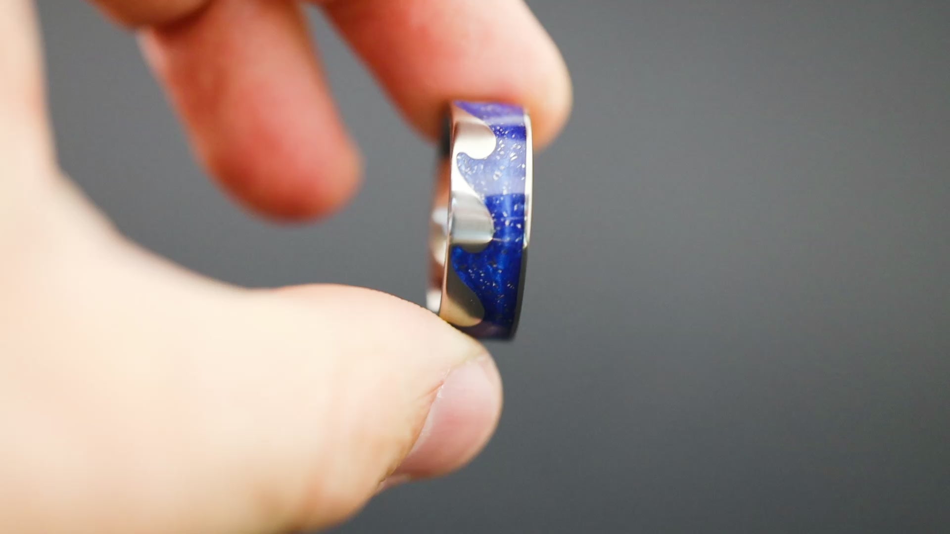 360 degree product view of the Blue Orbit Riptide ring showing Campo del Cielo meteorite pieces shifting through blue resin in wave-shaped cutout on 8mm titanium riptide band