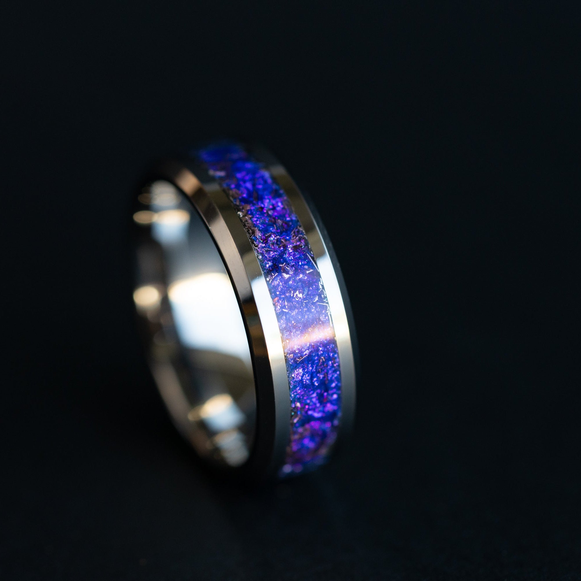 Close up of genuine Campo del Cielo meteorite shavings drifting through deep purple and blue midnight galaxy pigment inlay on 8mm beveled tungsten ring