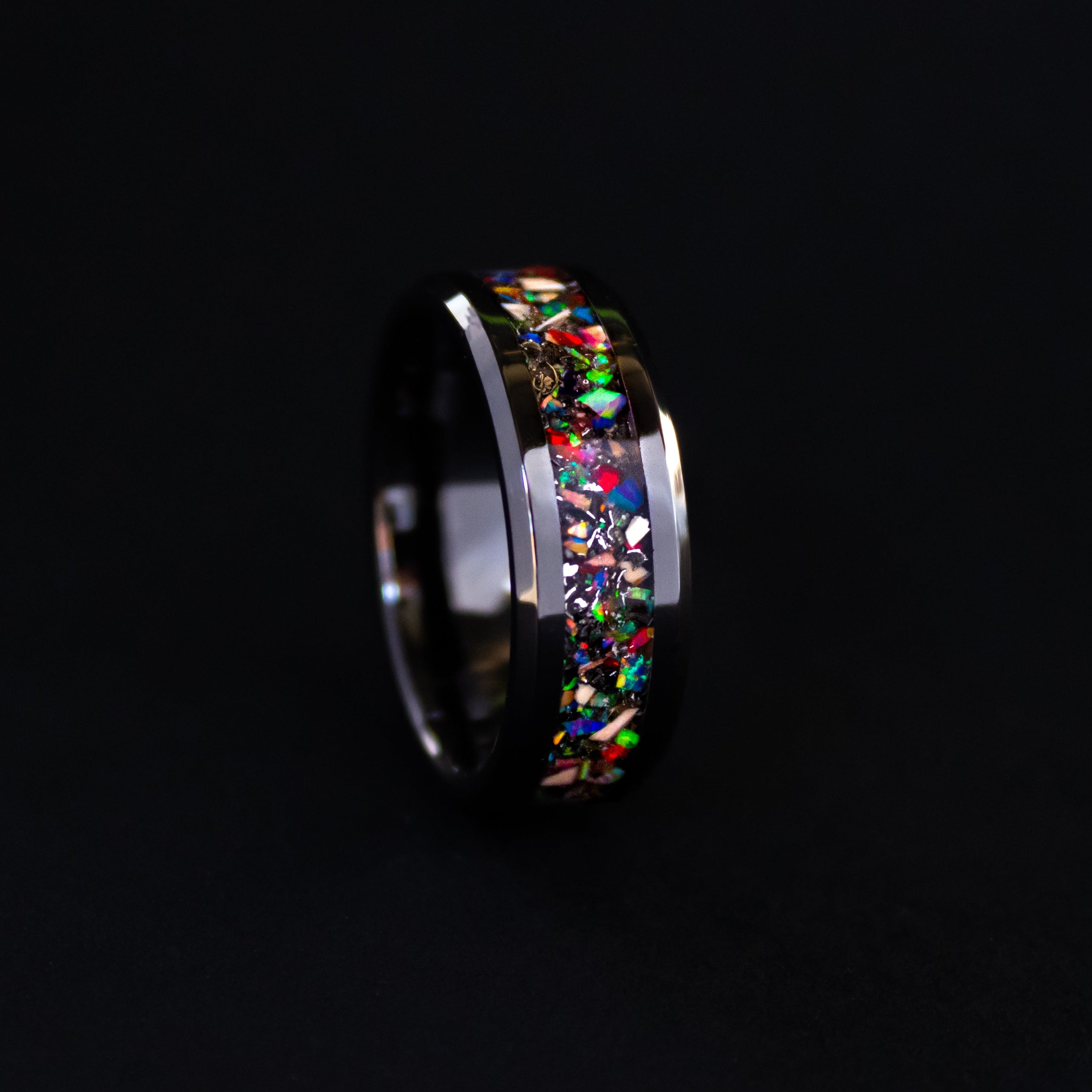 Detail shot of the Rainbow Mosasaur ring showing authentic Mosasaur bone fragments and multi-color opal pieces catching light on beveled black ceramic band
