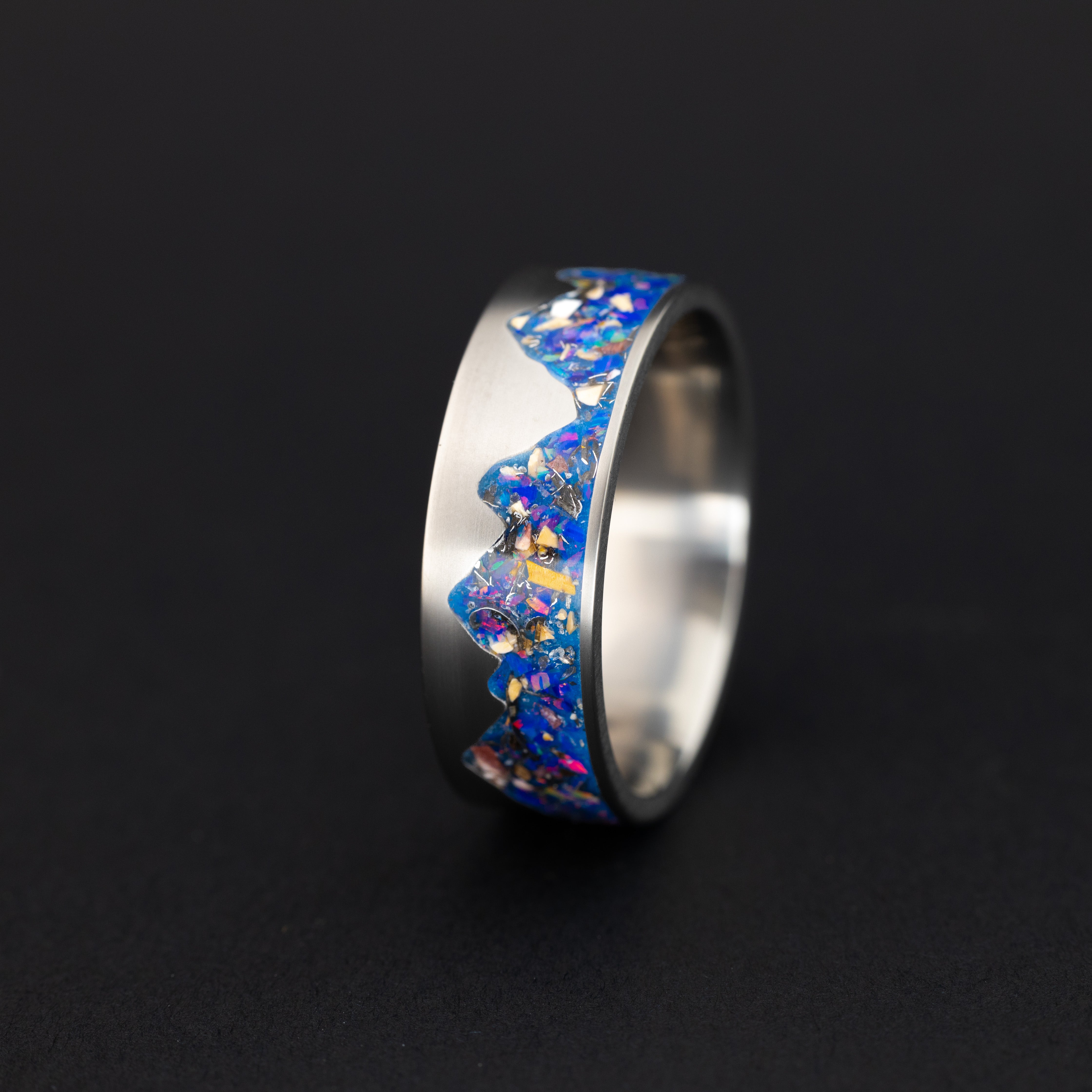 Titanium Raptor Ridgeline Glow ring with midnight opal, meteorite, and velociraptor fossil inlay in a mountain cutout.