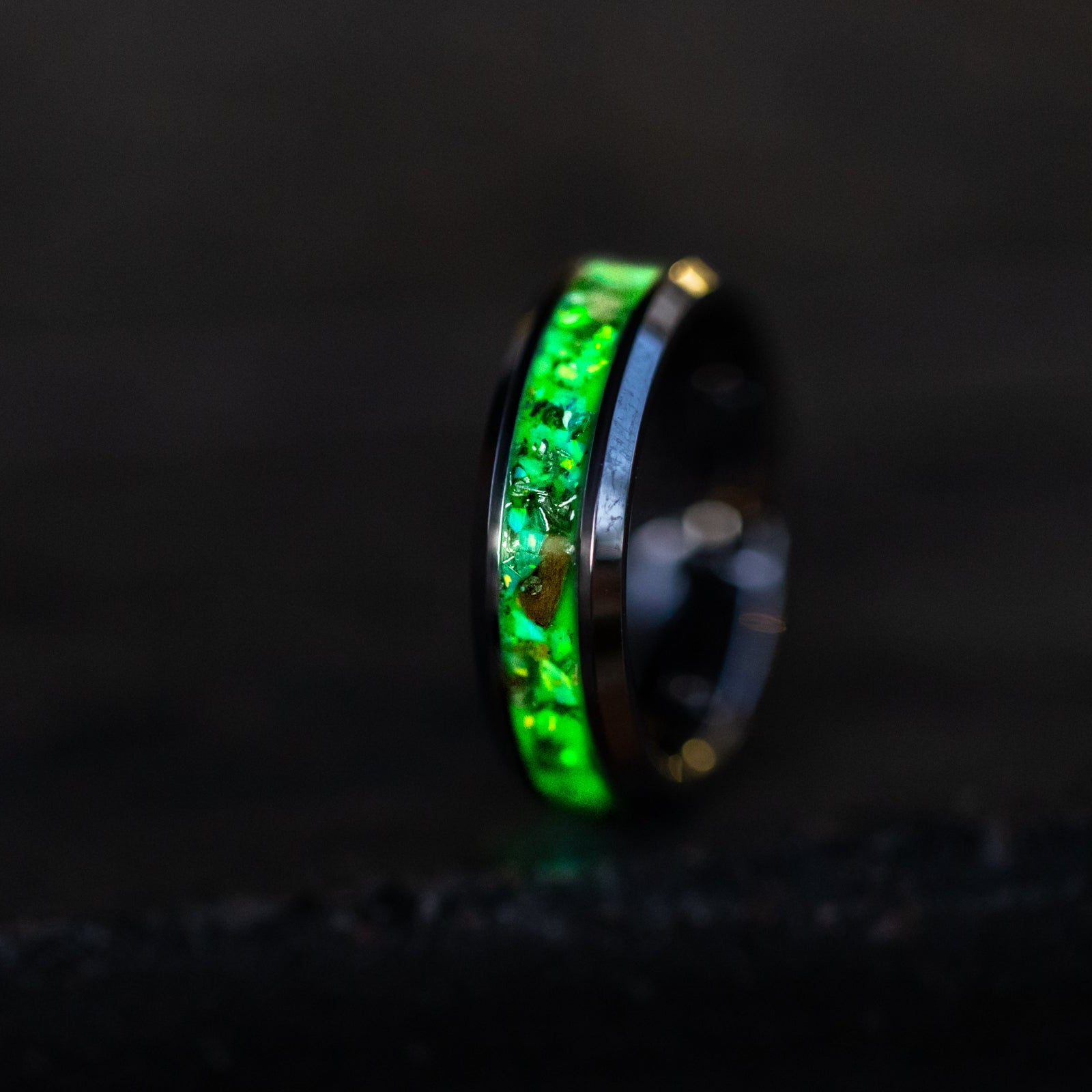 Toxic Raptor Tungsten ring glowing green in total darkness showing Velociraptor bone and meteorite suspended in electric green glow in the dark inlay