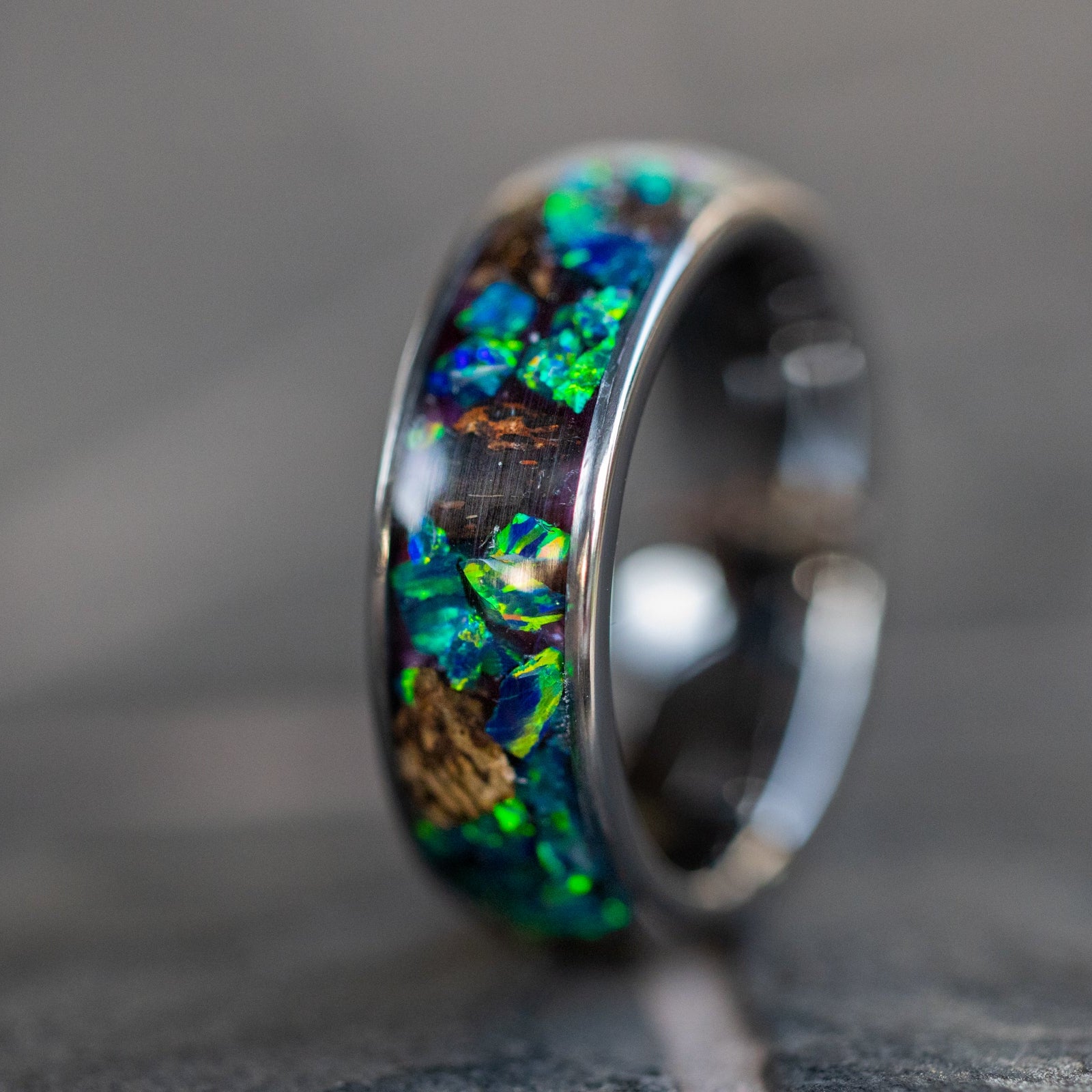 Close up of large genuine T-Rex fossil pieces surrounded by blue and green opal inlay on wide channel tungsten ring