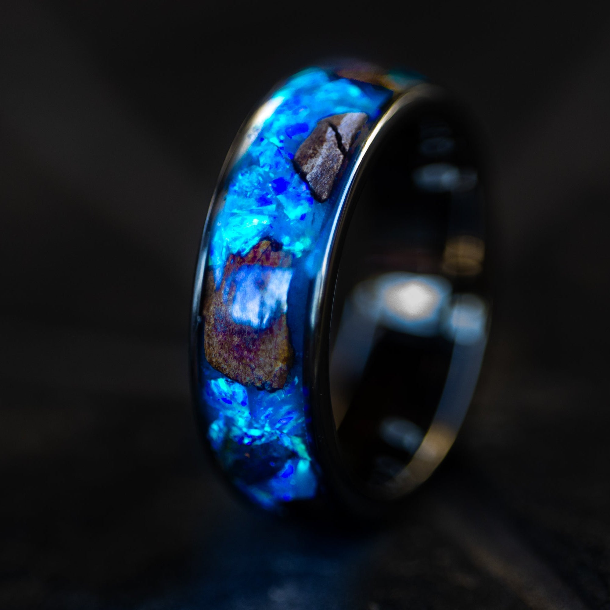 Close up of large genuine T-Rex fossil pieces and lunar meteorite chunks surrounded by blue opal inlay on wide channel tungsten ring