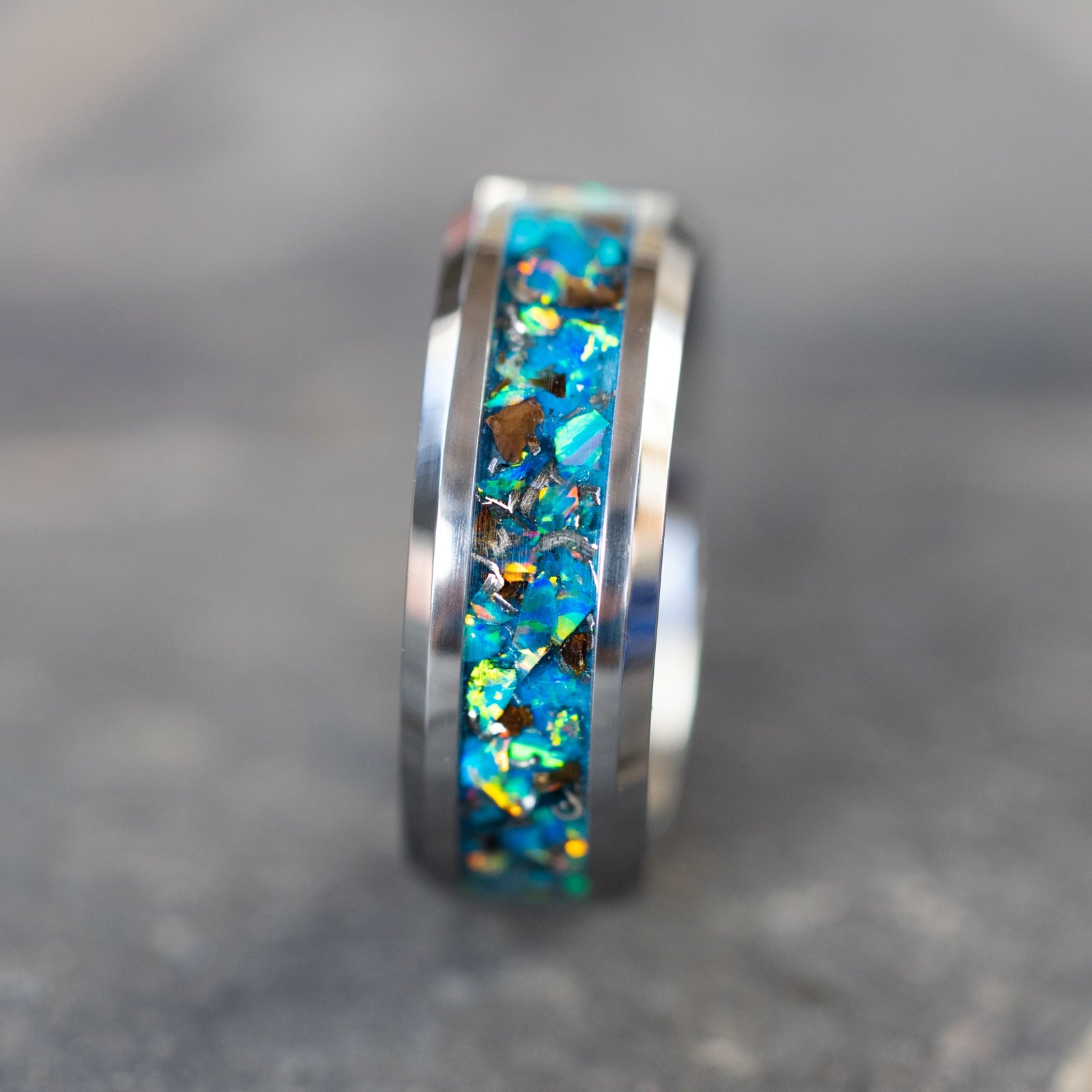 Close up of genuine T-Rex fossil and Campo del Cielo meteorite shavings suspended in light blue teal oasis opal inlay on beveled tungsten ring