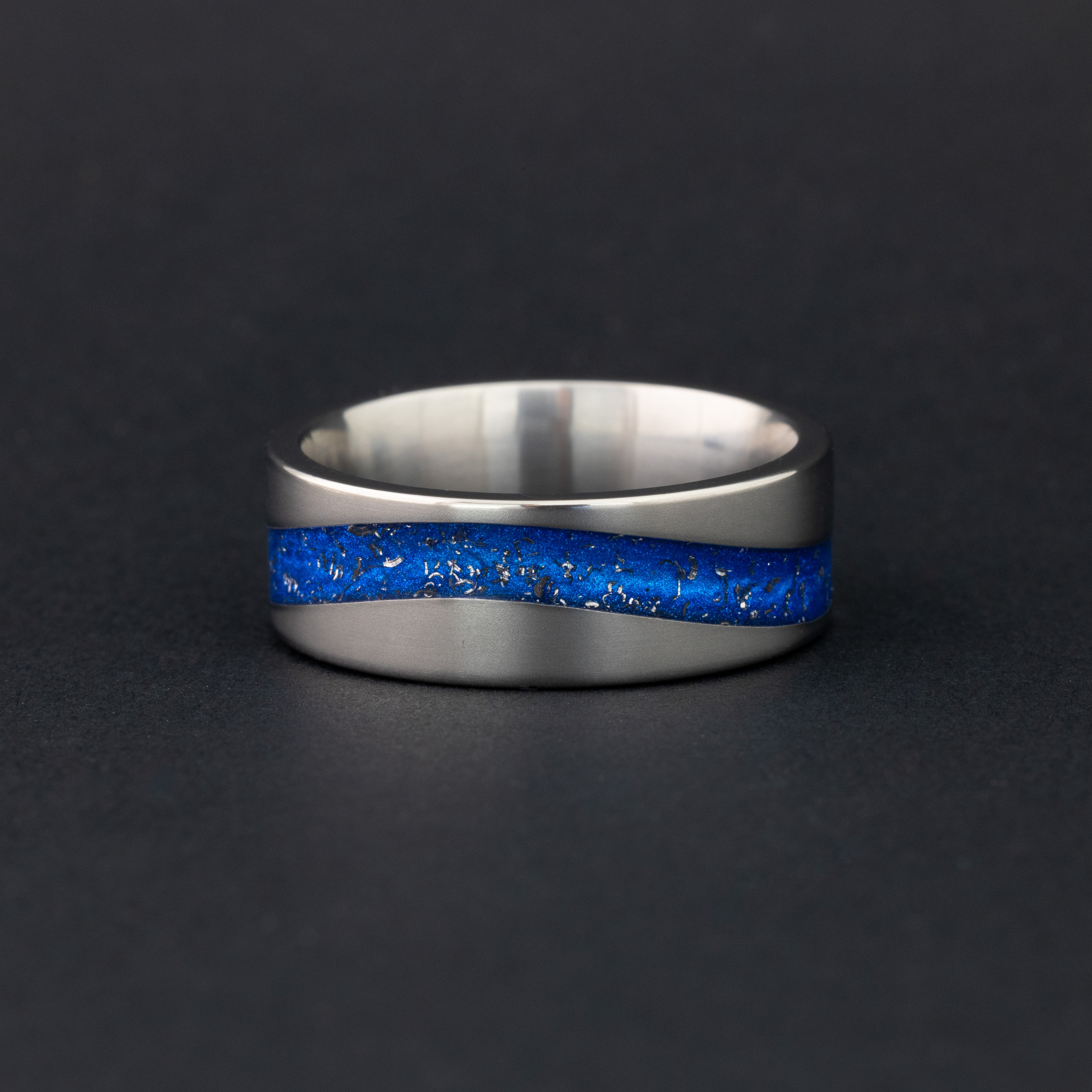Detail shot of the Blue Drift ring showing authentic Campo del Cielo meteorite pieces drifting through blue resin in curved inlay channel on tungsten band